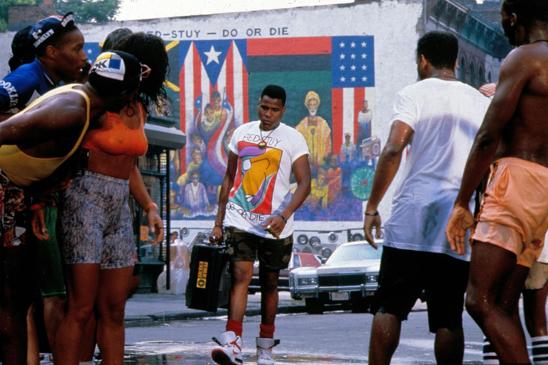 New York Street Style im Film „Do The Right Thing“ (1989): Radio Raheem (gespielt von Bill Nunn) trägt ein T-Shirt mit aufgedruckter Huldigung des Brooklyner Kiezes Bedford–Stuyvesant (Bed-Stuy), Camouflage-Shorts, rote Socken, Nike Air Revolution und einen gigantischen Ghettoblaster. Aus der Promax J-1 Super Jumbo ertönt „Fight the Power“ von Public Enemy als Kampfansage ans Establishment.