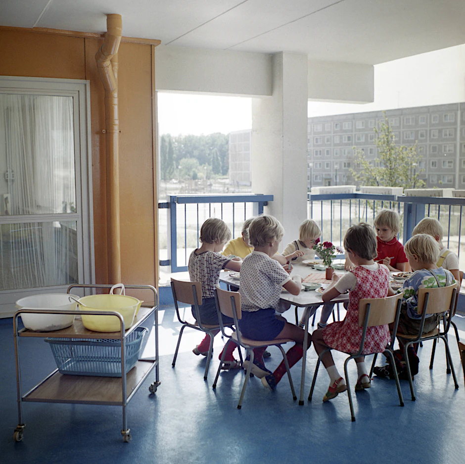 1976: Kinder einer Kindertagesstätte in der Lindenbergallee in Ost-Berlin sitzen zum Essen auf dem Balkon an einem Tisch.