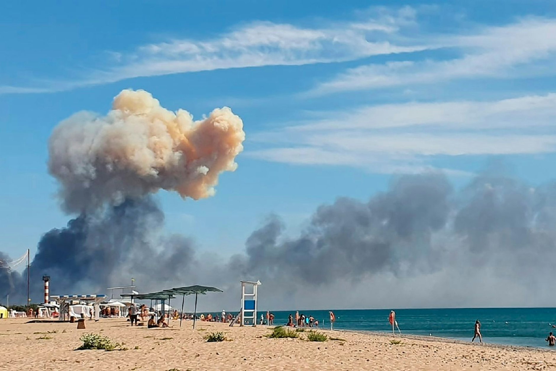 Urlauber am Strand der Krim, weit von der Front entfernt – und im Hintergrund steigt Rauch vom Luftwaffenstützpunkt Saki auf. Dort soll es einen Toten gegeben haben.