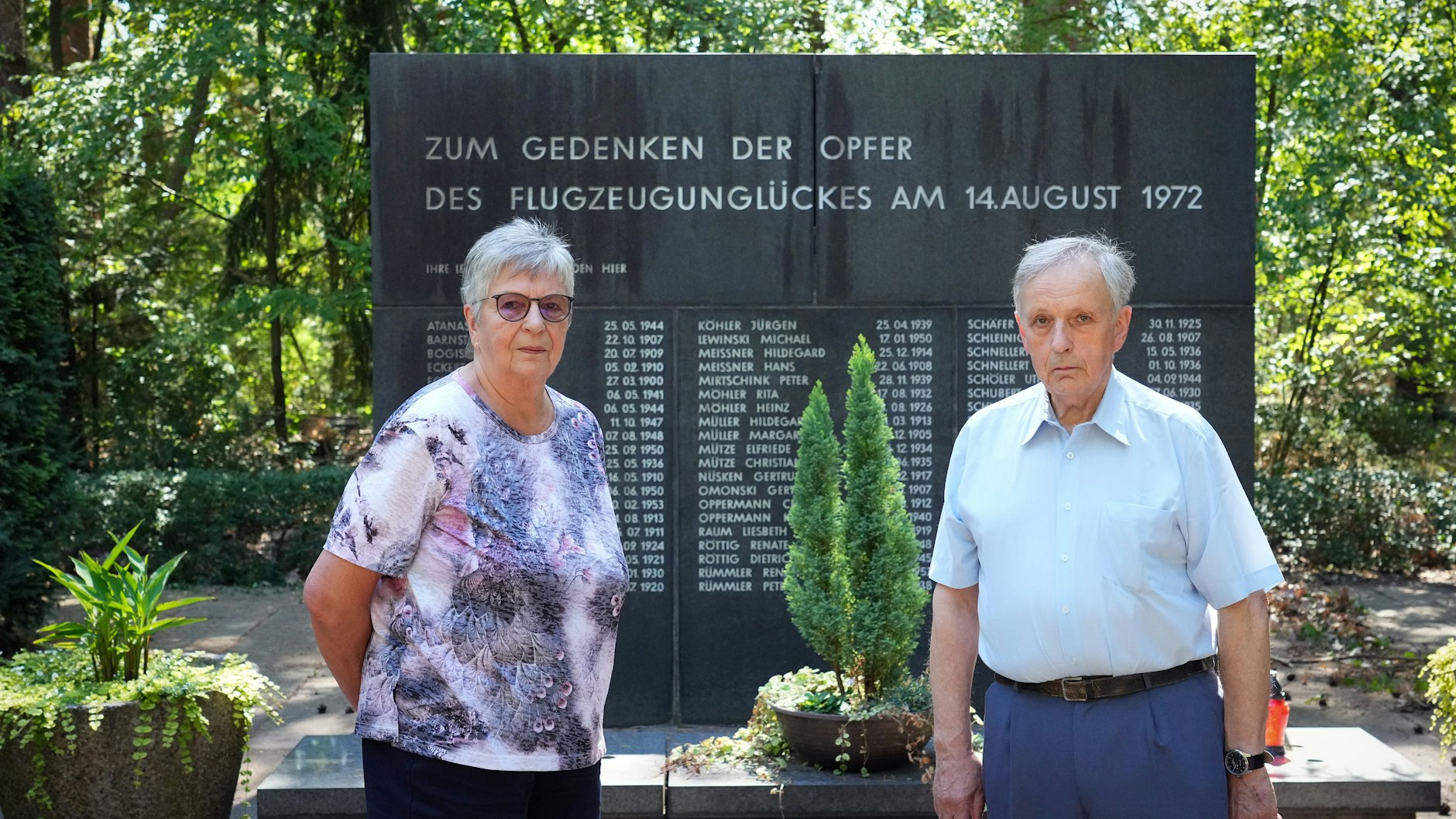 Zeitzeugin Ursula B. (l.) und Jörn Lehweß-Litzmann, damaliger Interflug-Ingenieur, stehen auf dem Waldfriedhof vor dem Gedenkstein für die Opfer des Flugzeugabsturzes von 1972.