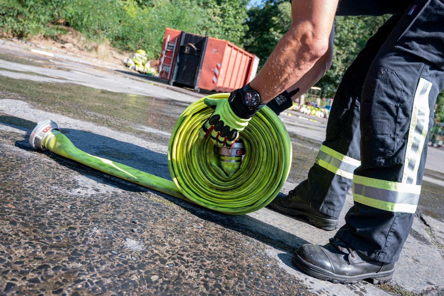Ein Mitarbeiter der Feuerwehr Berlin rollt nahe des Sperrgebiets um die Brandstelle am Sprengplatz der Berliner Polizei einen Feuerwehrschlauch zusammen.