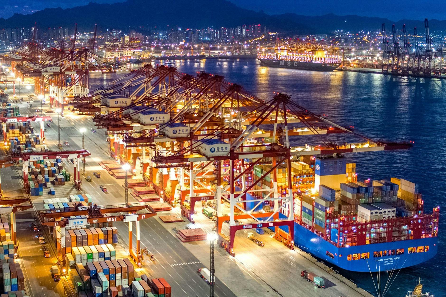 Containerschiffe liegen im nächtlich beleuchteten Containerterminal des Hafens von Qingdao.