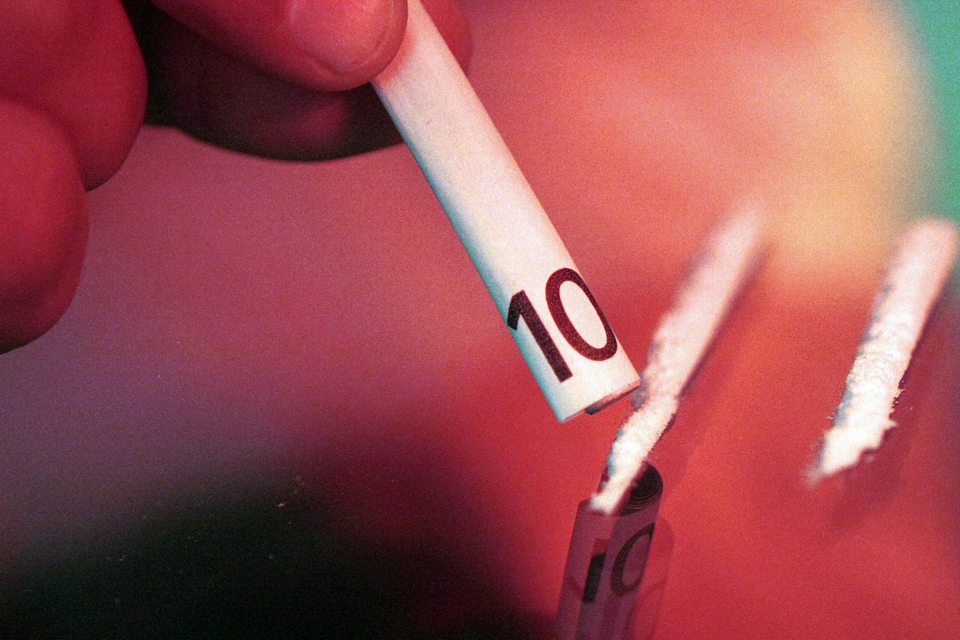 Drogenkonsumenten schnupft durch einen aufgerollten 10-Euro-Schein zwei auf dem Tisch vorbereitete Kokain-Linien