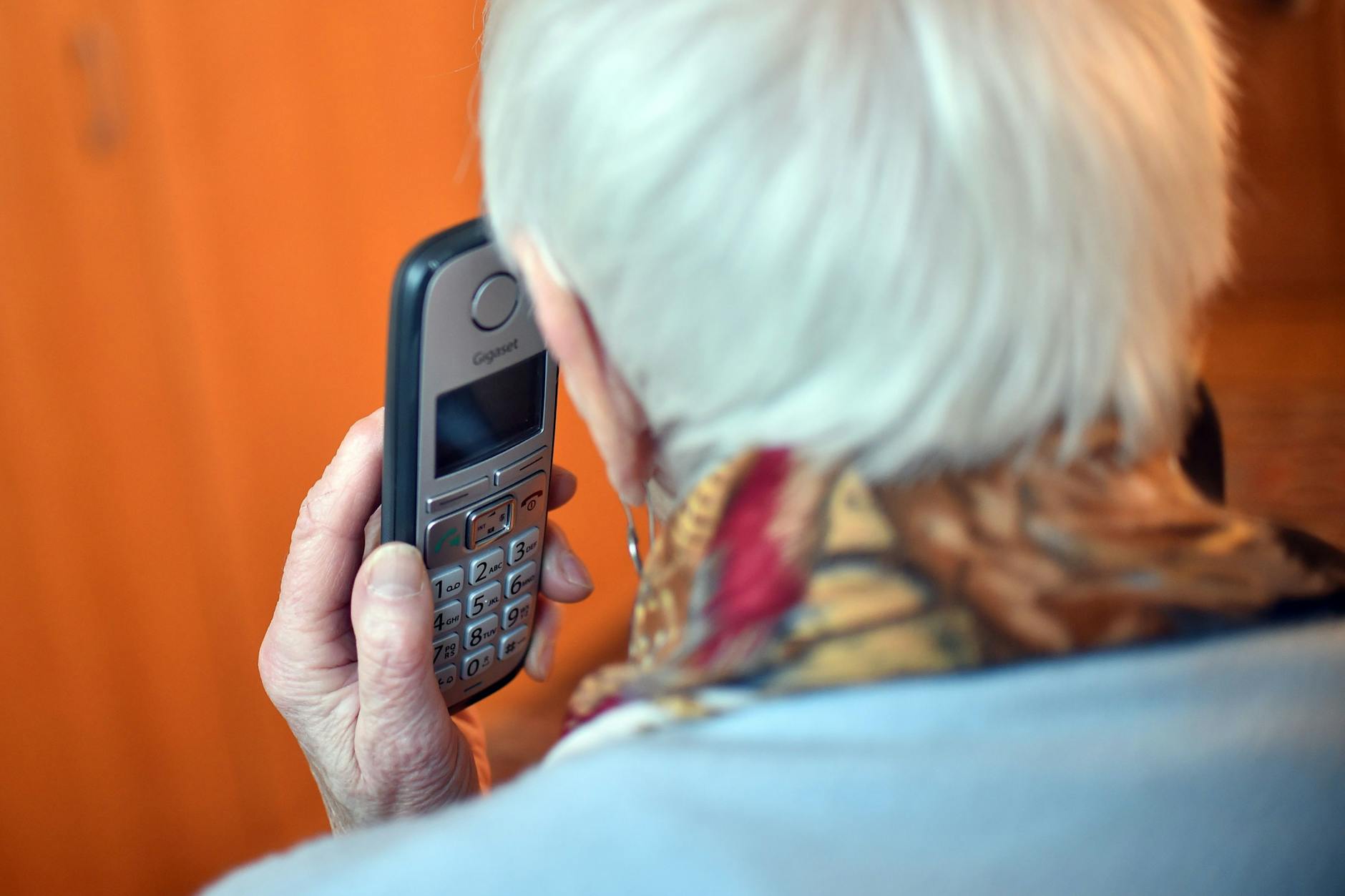 Eine Seniorin hält einen Telefonhörer an ihr Ohr.