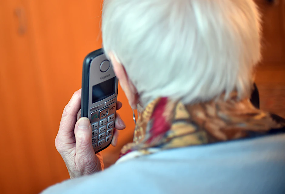 Eine Seniorin hält einen Telefonhörer an ihr Ohr.