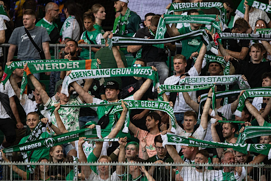 Fans von Werder Bremen stehen mit ihren Schals auf der Tribüne.  