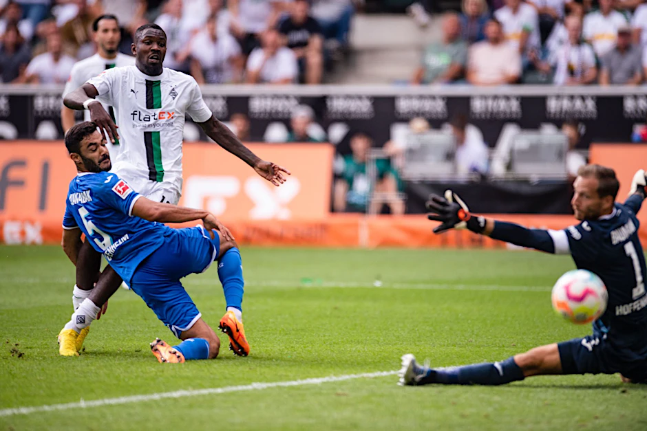 Gladbachs Marcus Thuram (M) trifft gegen Hoffenheims Ozan Kabak (l) und Torhüter Oliver Baumann zum 2:1.  