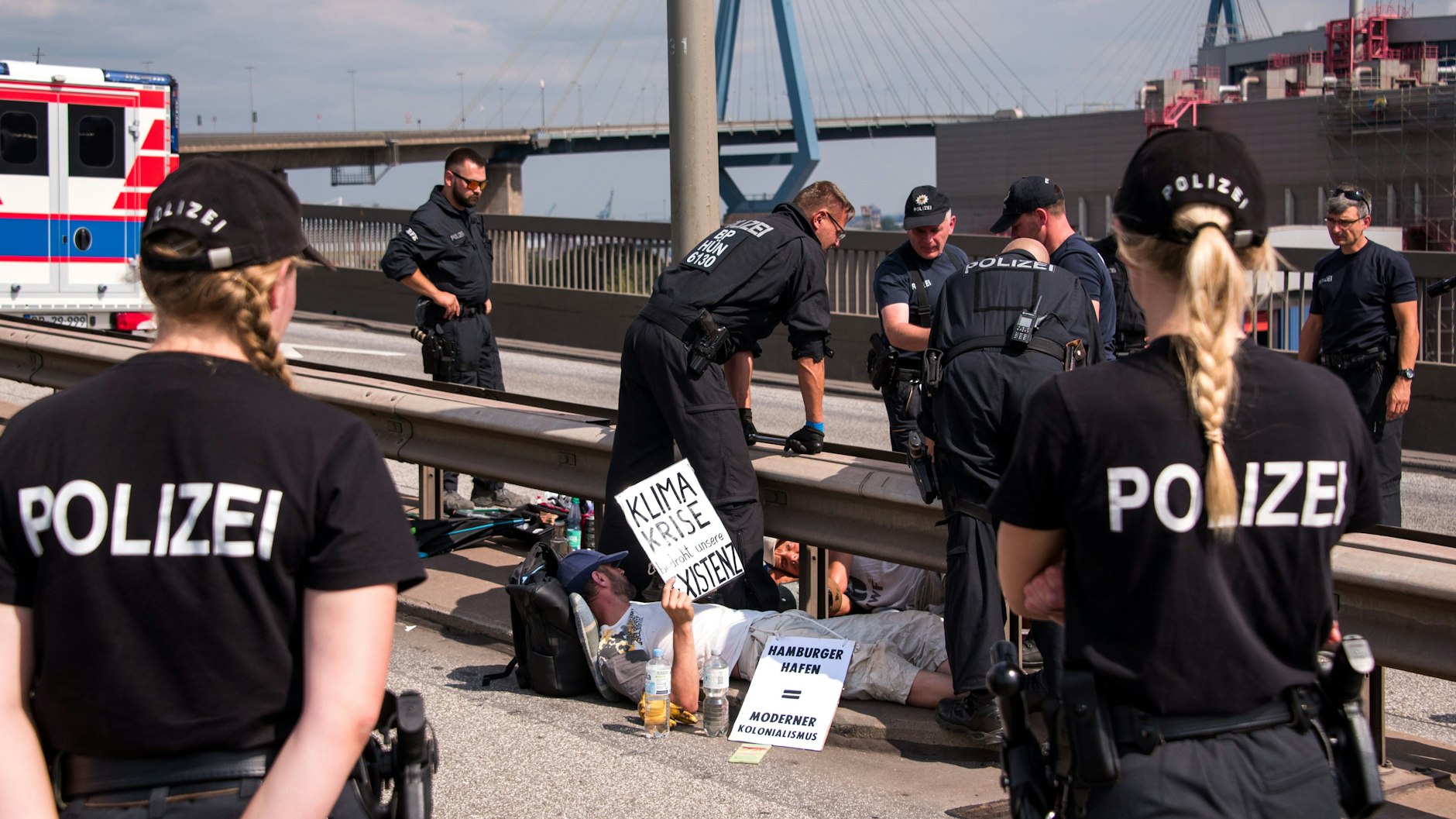 Polizisten versuchen auf der Köhlbrandbrücke, zwei mit einem Eisenrohr miteinander verbundene Demonstranten zu lösen.