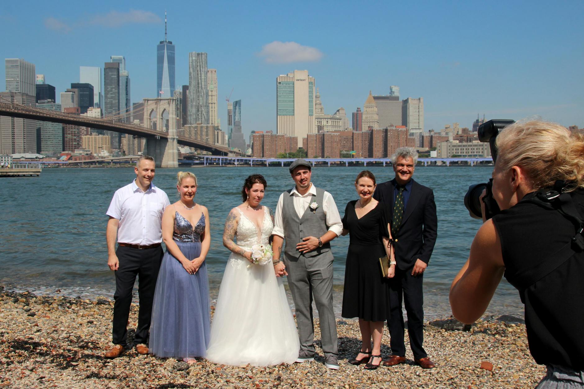 Ja-Wort mit Kulisse: Hochzeitsplaner Erol Inanc (2. v. r.) steht bei der Trauung von Annika Heisig (3. v. l.) und Patrick Brosch (4. v. l.) mit der Standesbeamtin (3. v. r.) und den Trauzeugen am Pebble Beach im Brooklyn Bridge Park für ein Gruppenfoto zusammen.