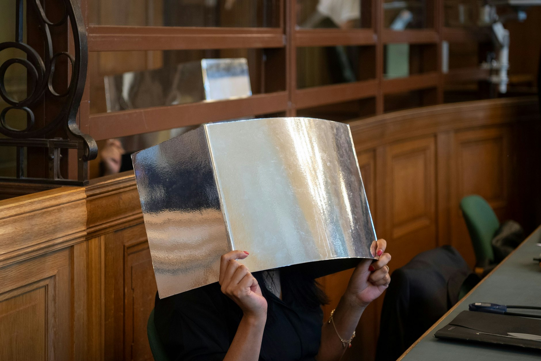 Berlin: Die Angeklagte hält sich in einem Gerichtssaal eine Pappe vor ihr Gesicht. Zusammen mit ihrem Bruder (hinten) muss sie sich wegen Betrugs in Berliner Corona-Testzentren in Millionenhöhe verantworten.