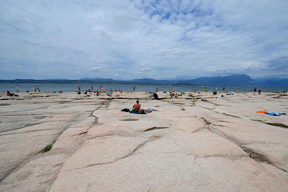 Menschen sonnen sich am Gardasee. Der Wasserstand ist nach einer Dürre stark gesunken, wodurch die Steine, die die Halbinsel von Sirmione umgeben, freigelegt wurden.