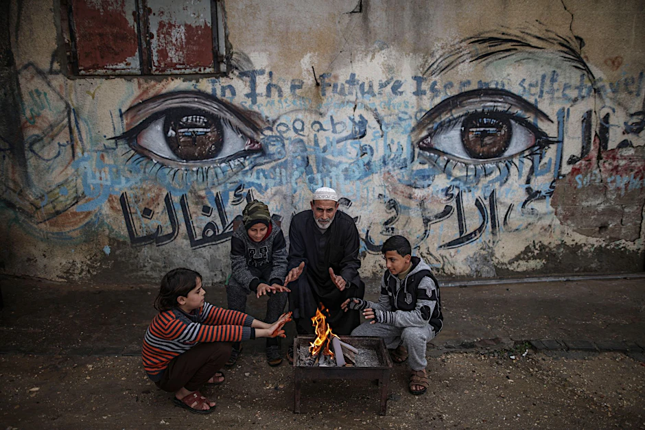 ARCHIV - Palästinensische Kinder wärmen sich mit ihrem Großvater an einem Feuer in Gaza-Stadt (Archiv).  