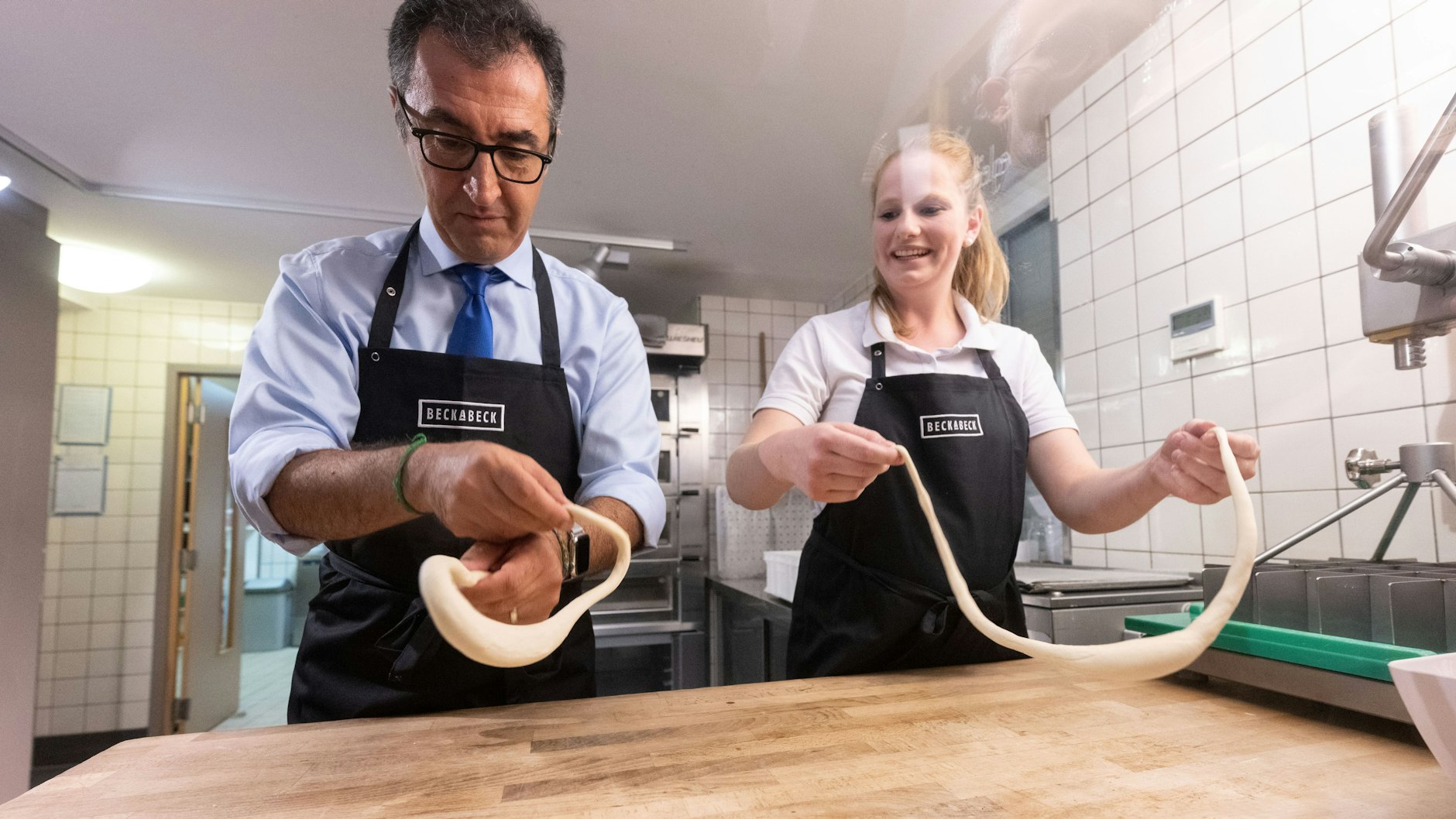 Gar nicht so leicht! Minister Cem Özdemir versucht sich in der&nbsp;Großbäckerei BeckaBeck am Brezel formen.&nbsp;&nbsp;Neben ihm Luisa Beck, Tochter des Bäckerei-Chefs.&nbsp;