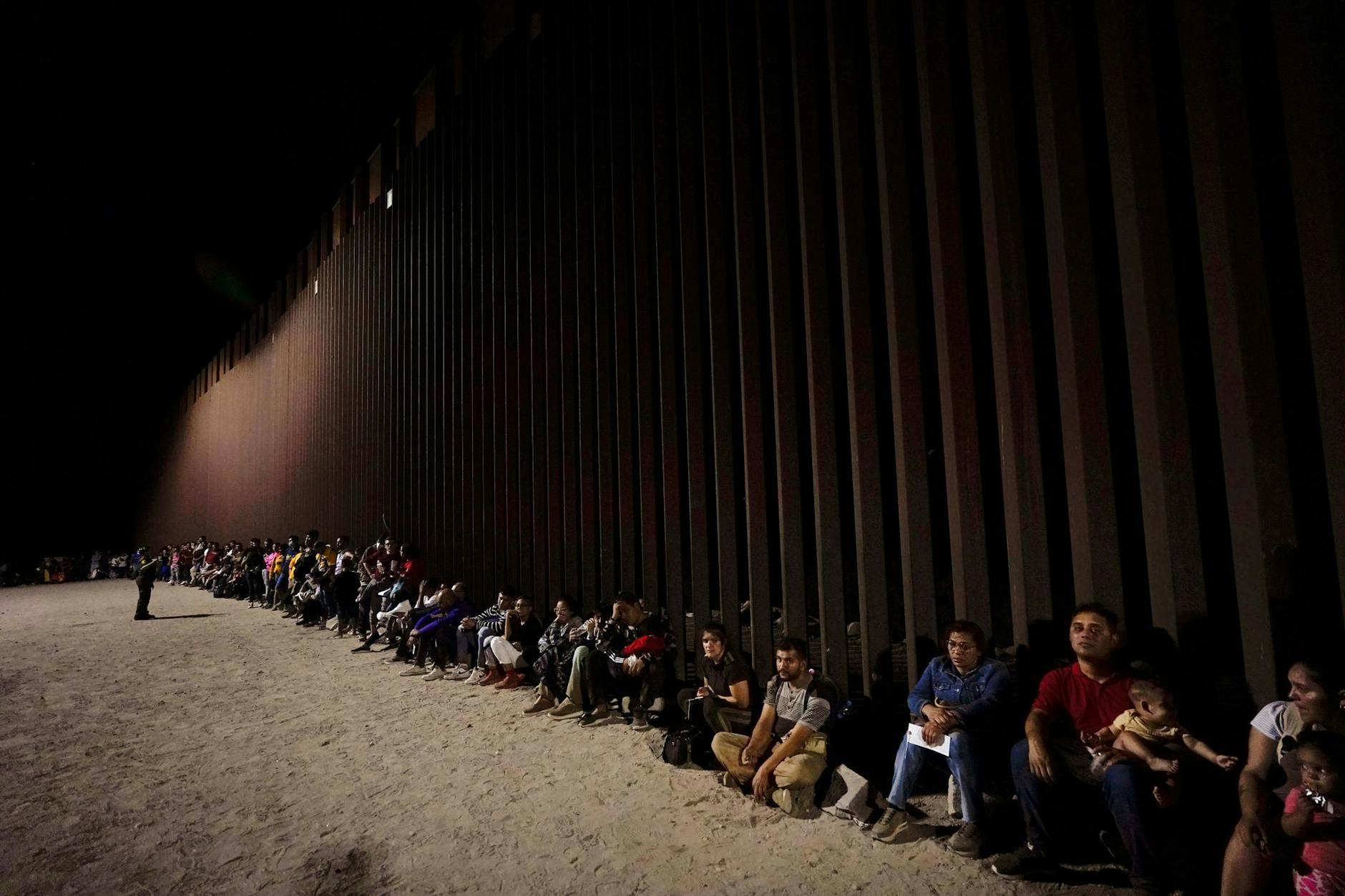 dpatopbilder - Migranten warten entlang einer Grenzmauer, nachdem sie die Grenze von Mexiko in der Nähe von Yuma im US-Bundesstaat Arizona überquert haben.