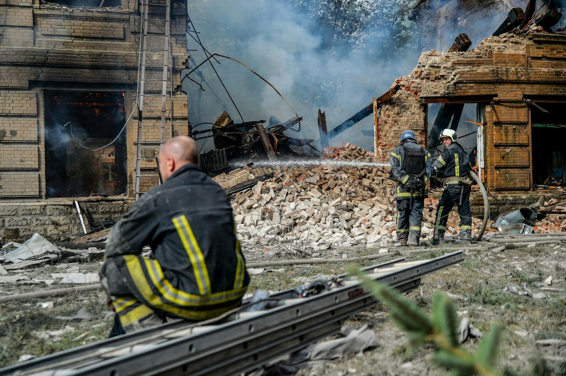 Ein Feuerwehrmann macht eine Verschnaufpause, während zwei seiner Kollegen vor einem zerstörten Gebäude der Chemisch-Mechanischen Hochschule in Slowjansk ein Feuer löschen. ZUMA Press Wire/dpa