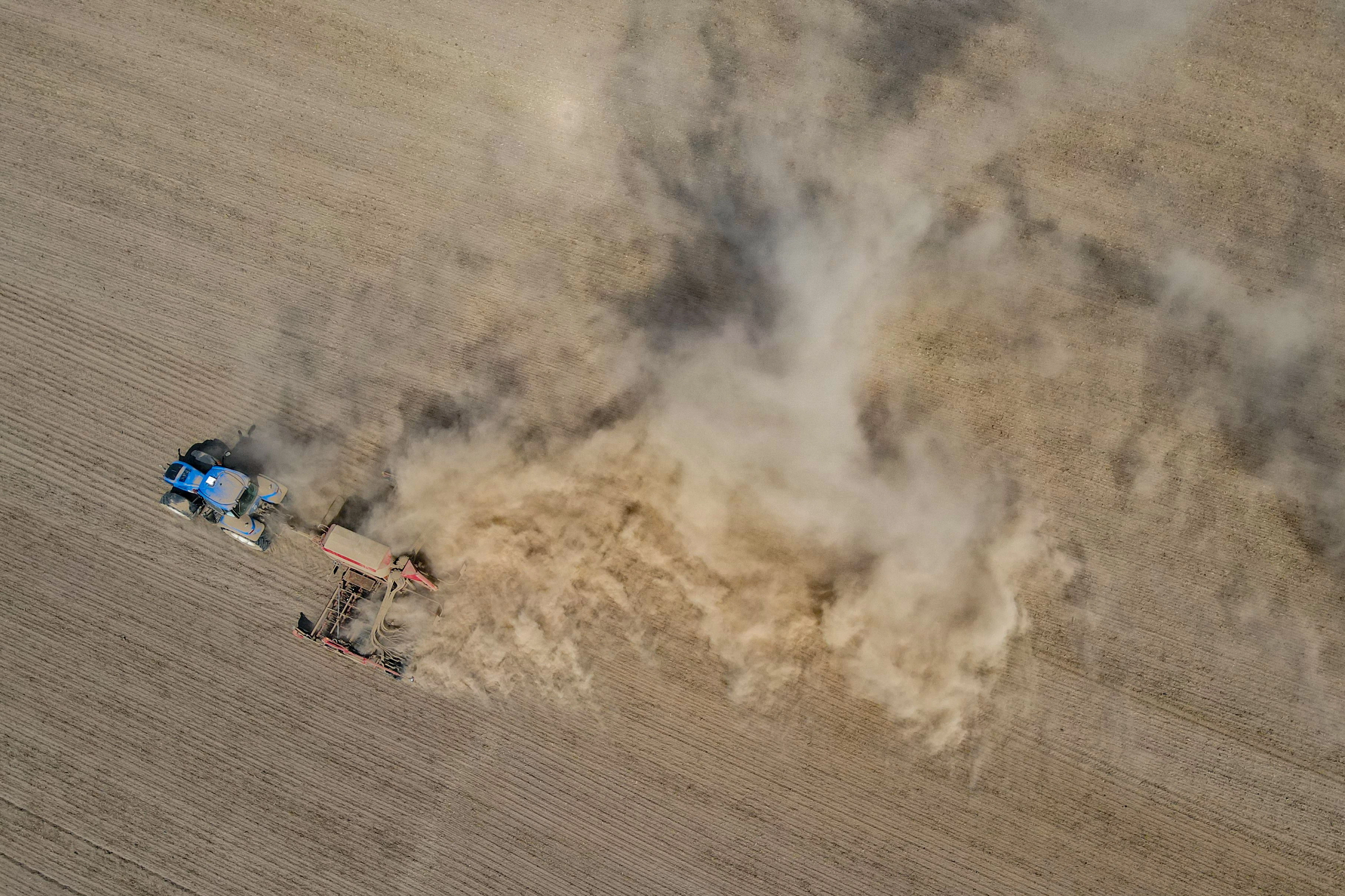 Ein Landwirt fährt mit einem Traktor und einer Drille über den trocken Ackerboden.