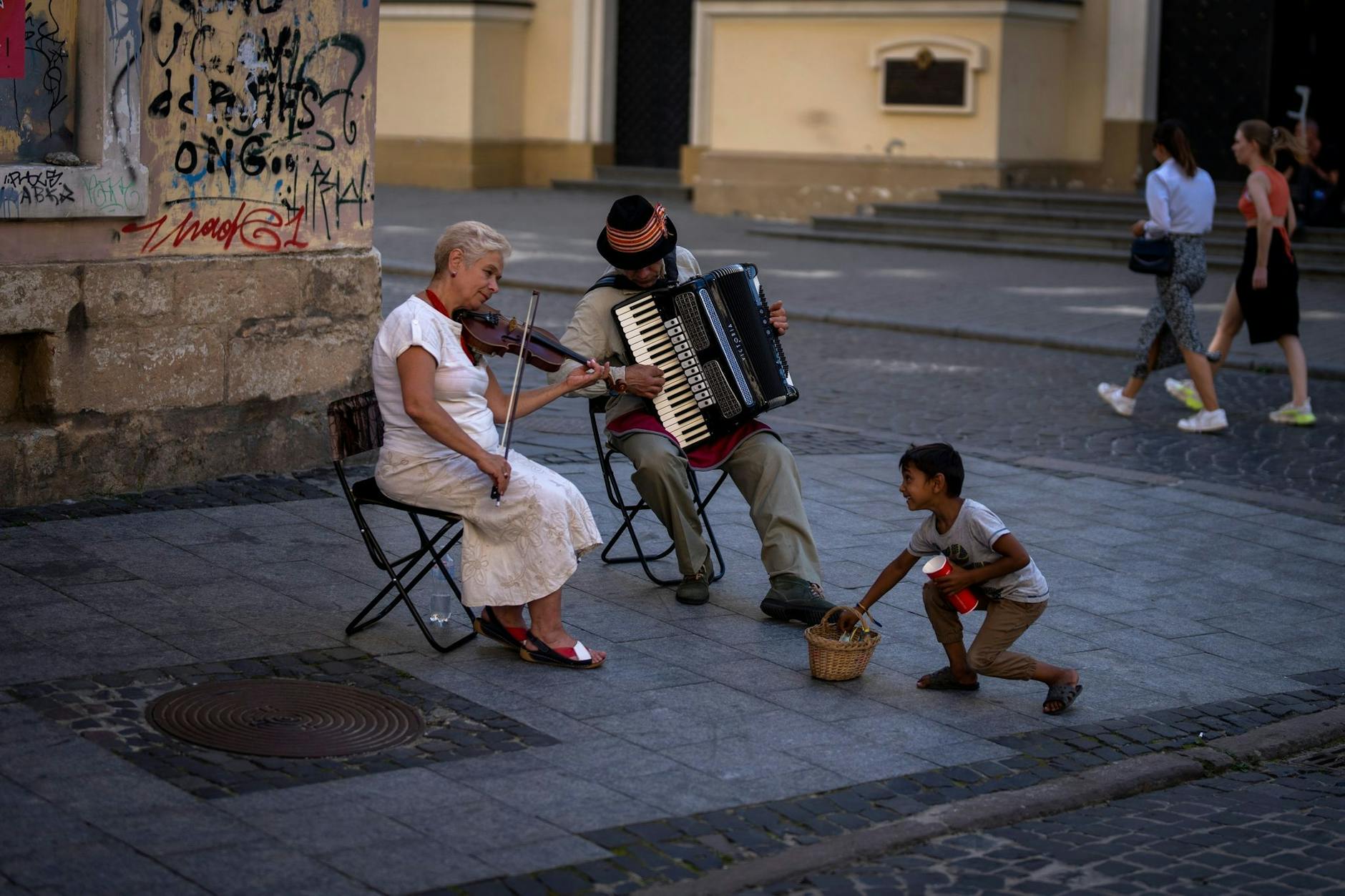 Ein Kind versucht, zwei Straßenmusikern in der Innenstadt von Lwiw Geld zu stehlen.