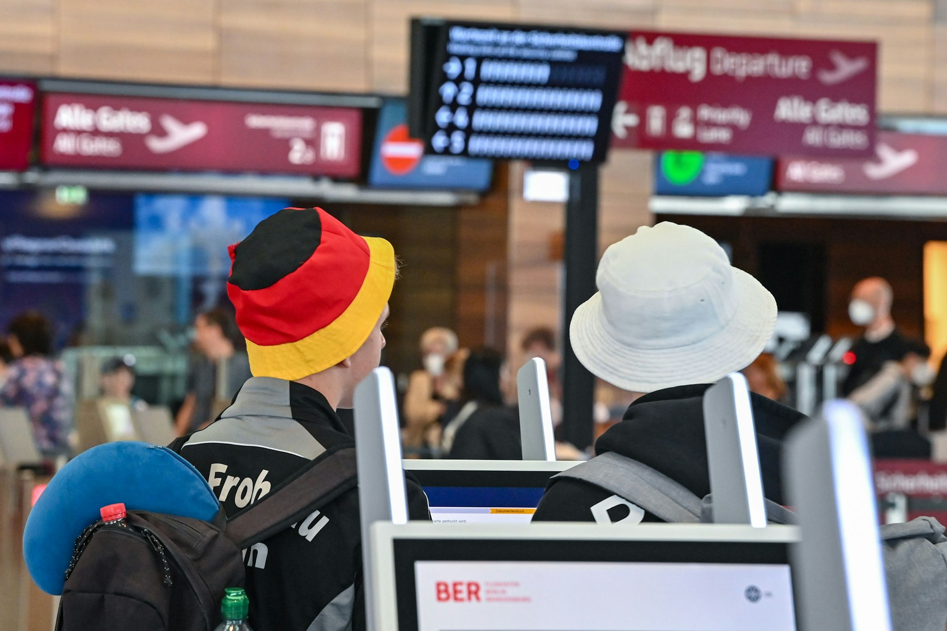 Reisende warten an einem Check-in für ihren Abflug vom Hauptstadtflughafen Berlin Brandenburg (BER). In Flugzeugen, die von Deutschland aus abfliegen, gilt weiterhin die Maskenpflicht.