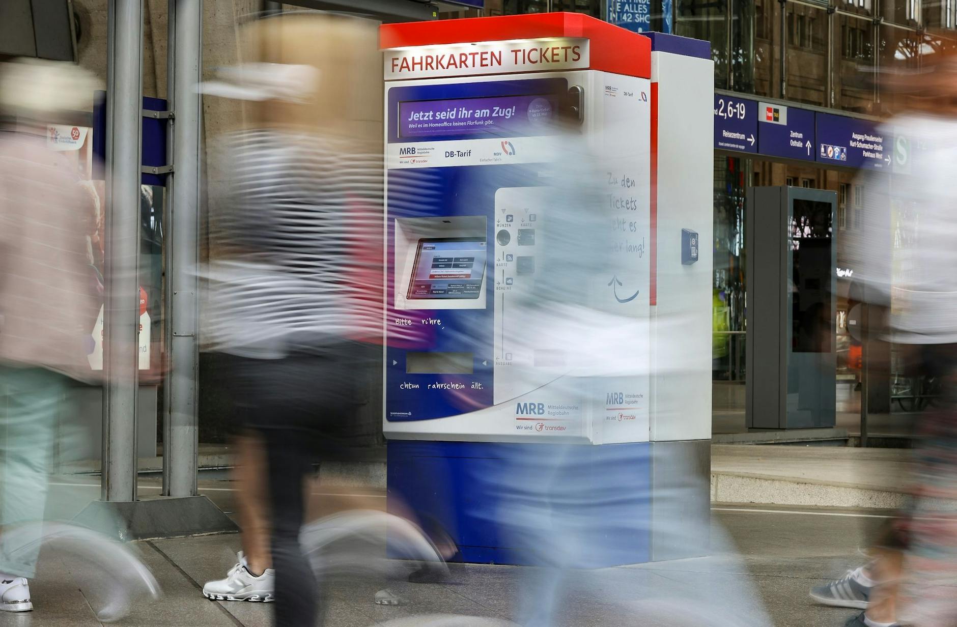 Passagiere gehen an einem Bahnhof an Fahrkartenautomaten vorbei.