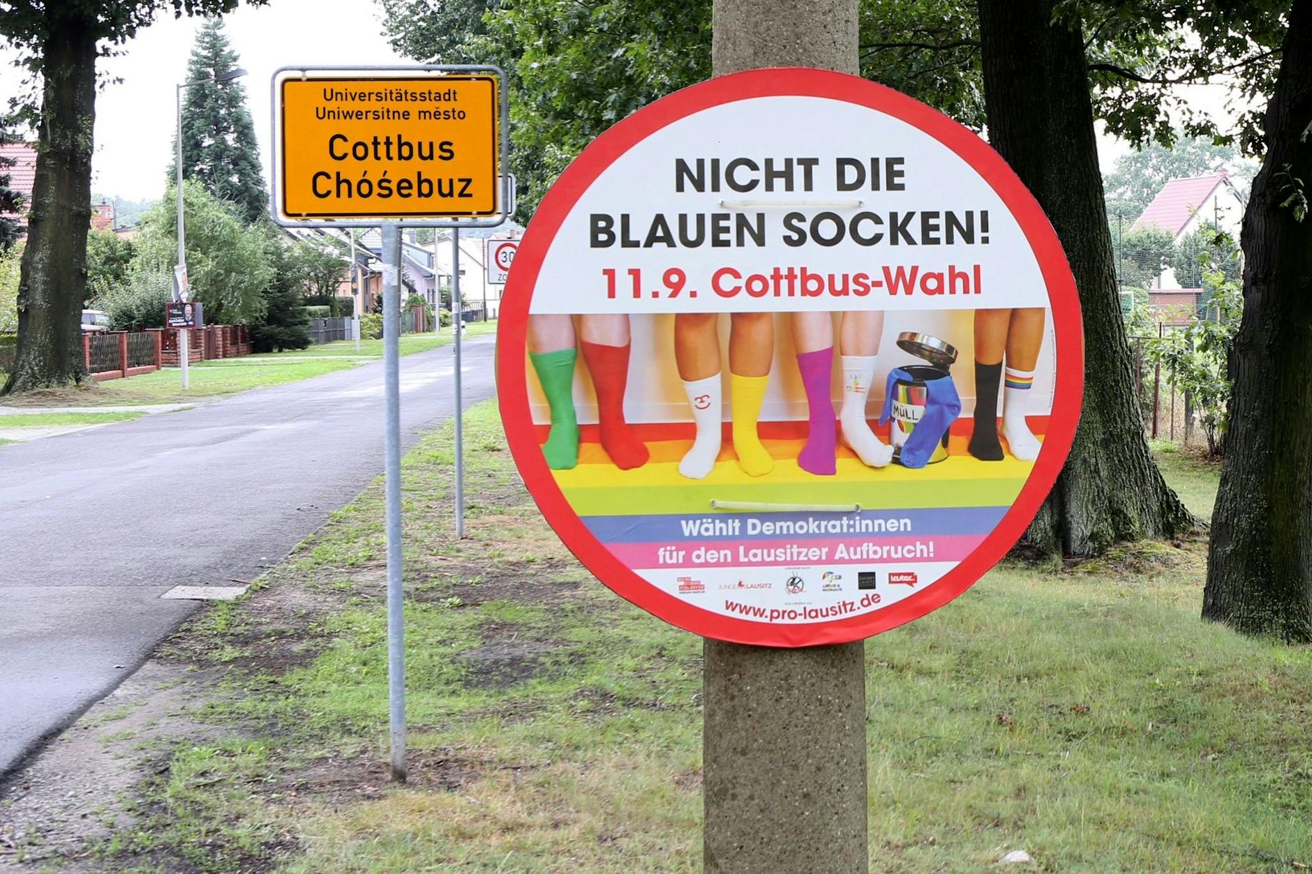 HANDOUT - Vor dem Ortseingangsschild der Stadt Cottbus hängt an einem Pfahl ein Plakat der Kampagne «Blaue Socken». a