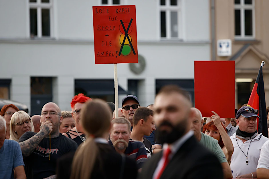 ARCHIV - Zuschauer protestieren bei einer Veranstaltung mit Bundeskanzler Olaf Scholz in Neuruppin.  