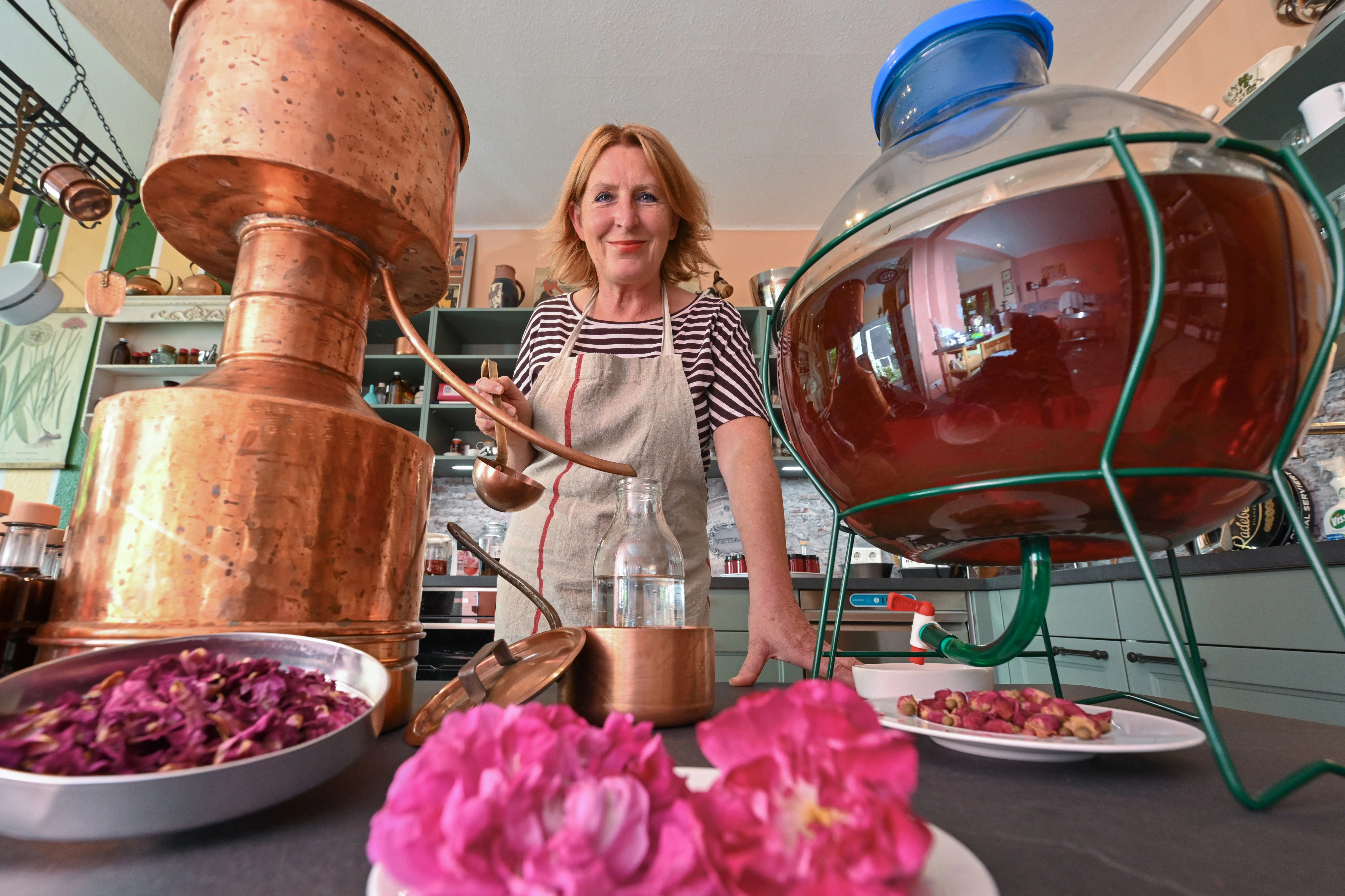 Elena von Gieck, Inhaberin des Rosenlaboratoriums Templin, steht in ihrem Laboratorium hinter getrockneten und frischen Rosenblättern und einer kupfernen Destille.