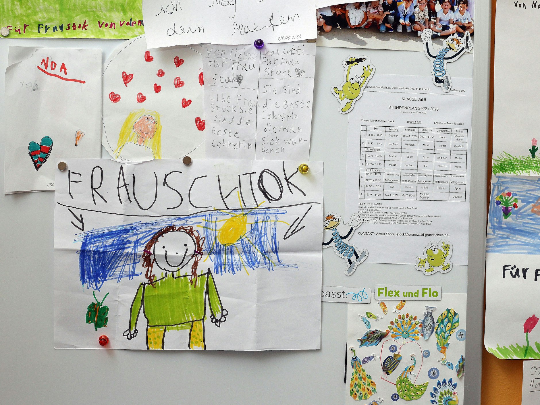 Kinder haben Bilder von ihrer Lehrerin gemalt. Auf dem einen Bild hat das mit der Schreibung des Namens fast schon hingehauen.