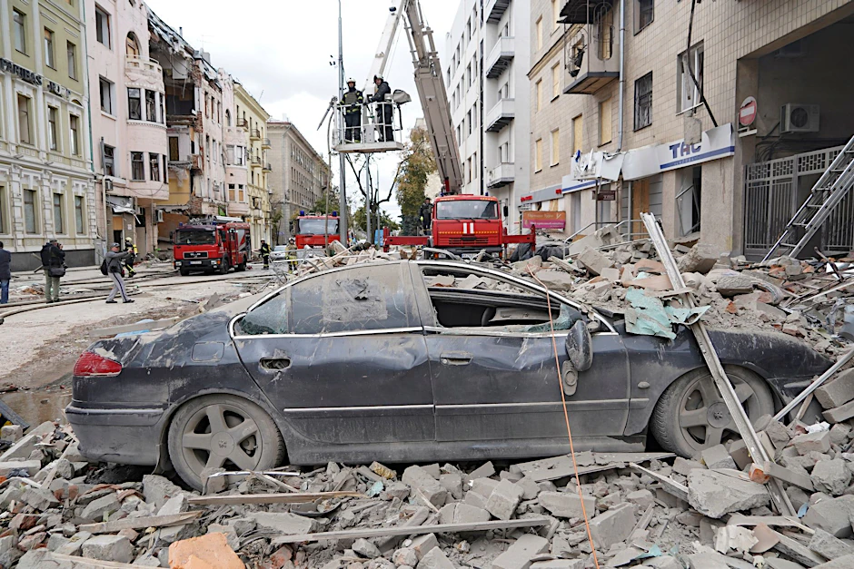 Feuerwehrleute stehen nach einem Raketenangriff des russischen Militärs auf einem Kran auf einer Straße in Charkiw.