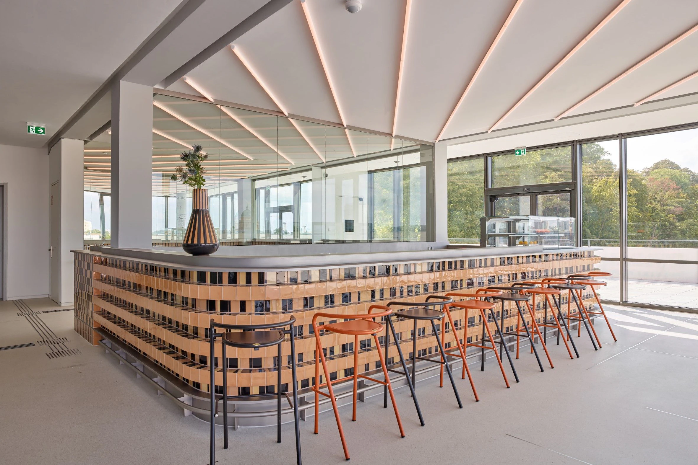 Ein erster Blick ins Innere: Die Cafébar im ersten Stock befindet sich an derselben Stelle wie die ursprüngliche Bar. Die Gestaltung mit handgefertigten Kacheln aus den Hedwig-Bollhagen-Werkstätten im brandenburgischen Marwitz ist nicht original; sie beruht auf einem Entwurf des Architekturbüros Linearama aus Genua.
              
              