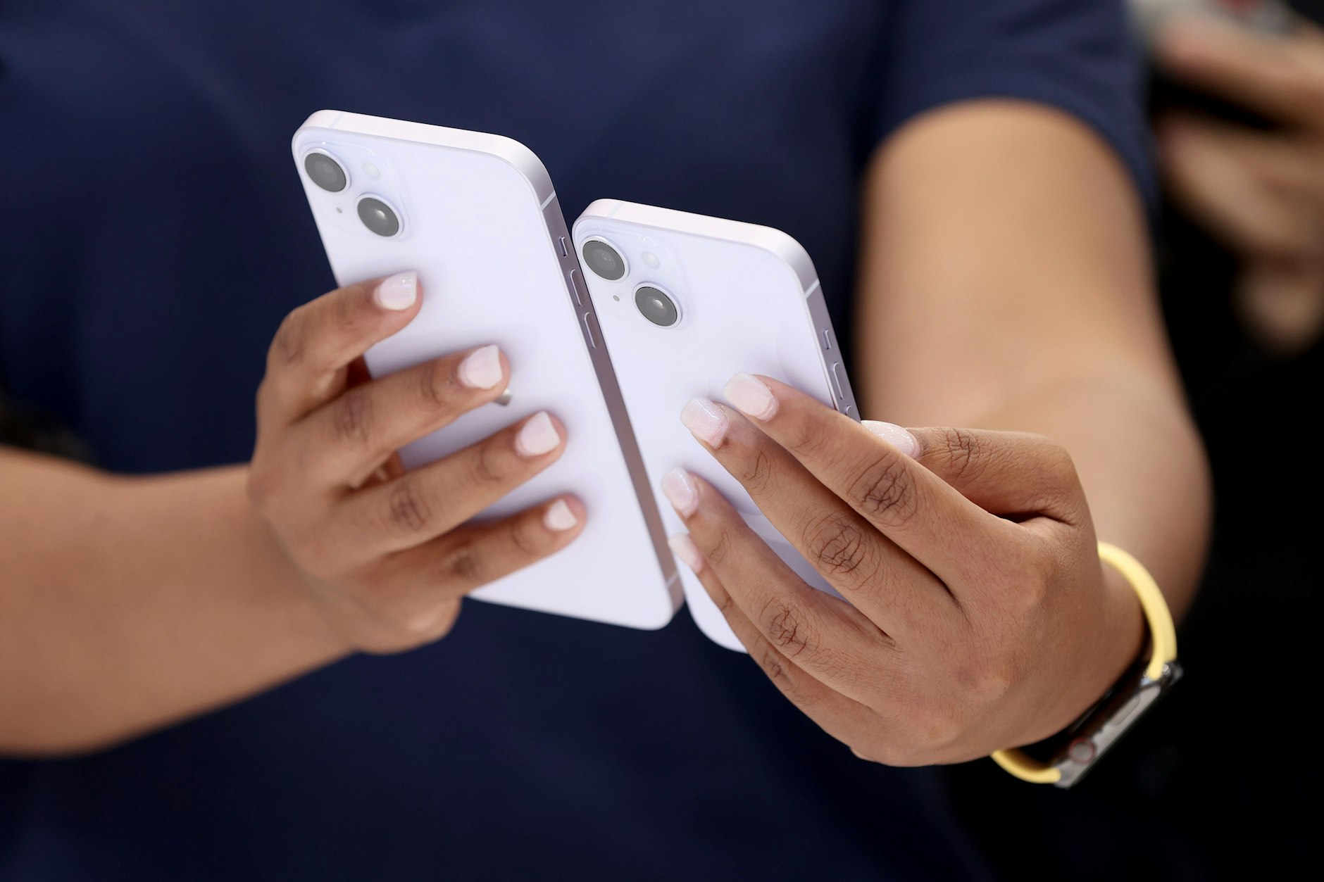 Eine Apple-Angestellte hält die iPhone-Modelle 14 und 14 Pro nebeneinander.