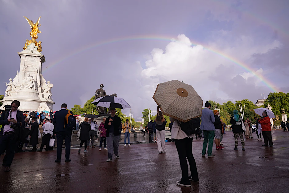 Ein Regenbogen ist über dem Queen Victoria Memorial zu sehen, während sich Personen vor dem Buckingham Palace versammeln.