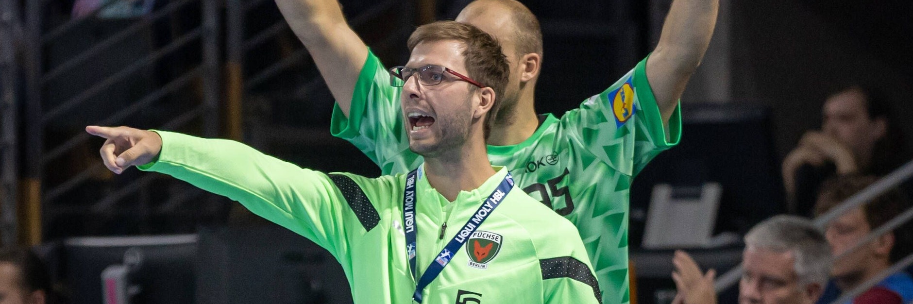 Trainer Jaron Siewert dirigiert gegen Stuttgart wieder von der Bank aus seine Füchse, hinter ihm jubelt Kapitän Paul Drux.