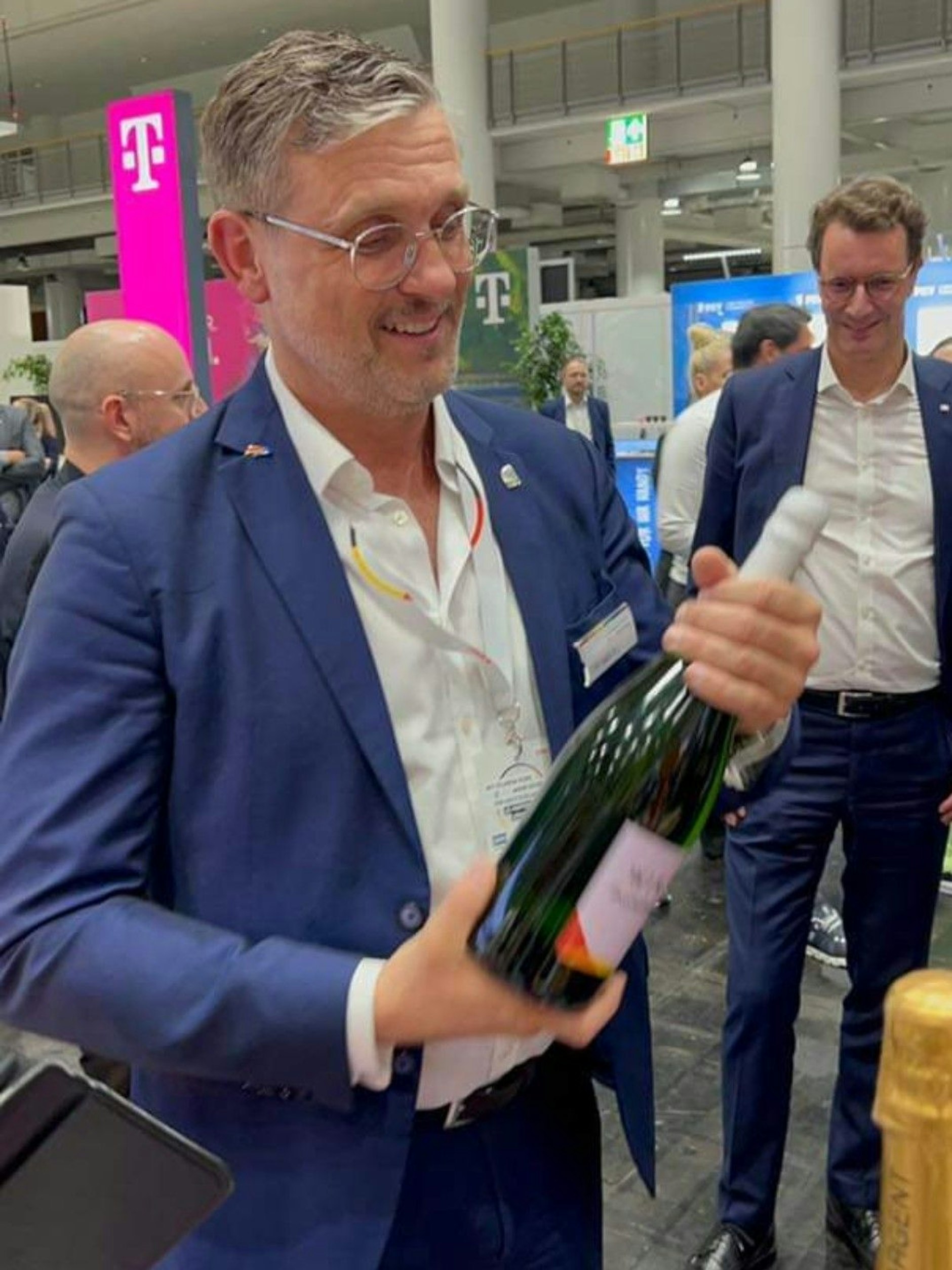 LSU-Bundesvorsitzender Alexander Vogt  lässt den Erfolg mit einer Flasche Sekt begießen. Auch NRW-Ministerpräsident Hendrik Wüst feiert mit.