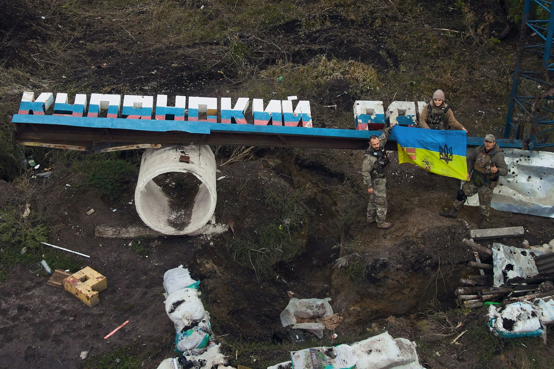 Ukrainische Soldaten halten eine ukrainische Fahne auf dem beschädigten Schild "Bezirk Kupiansk" in der Nähe der kürzlich zurückeroberten Stadt Kupjansk in der Region Charkiw.&nbsp;