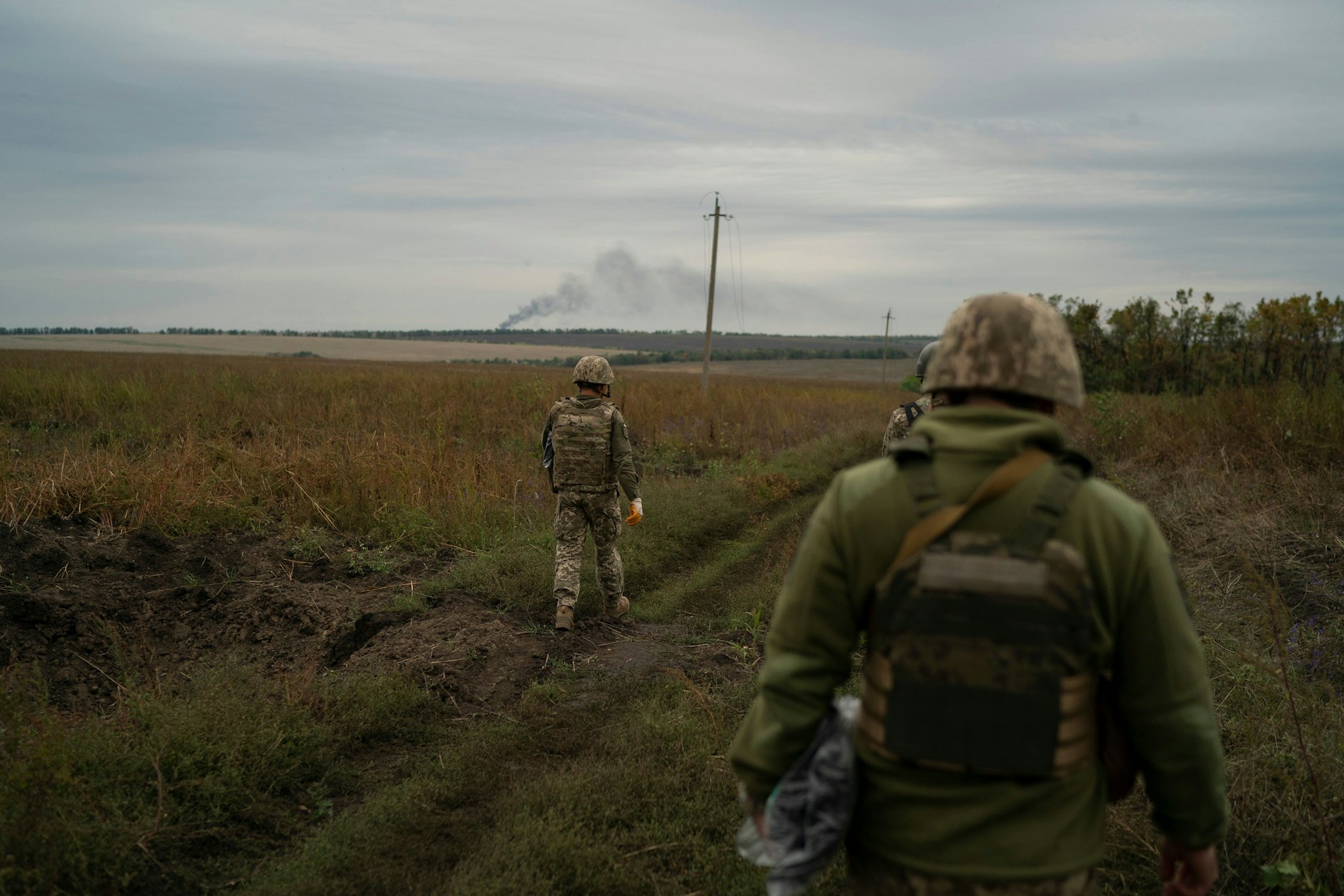 Ukrainische Soldaten gehen auf einem Feld, um die Leiche eines ukrainischen Soldaten in einem zurückeroberten Gebiet nahe der Grenze zu Russland in der Region Charkiw zu bergen. 