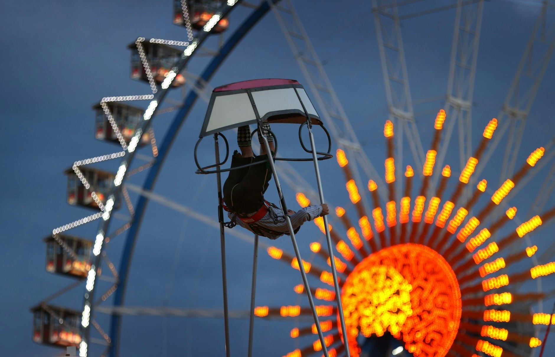 Ein junger Mann schaukelt in der Schiffschaukel vor dem Riesenrad.  
