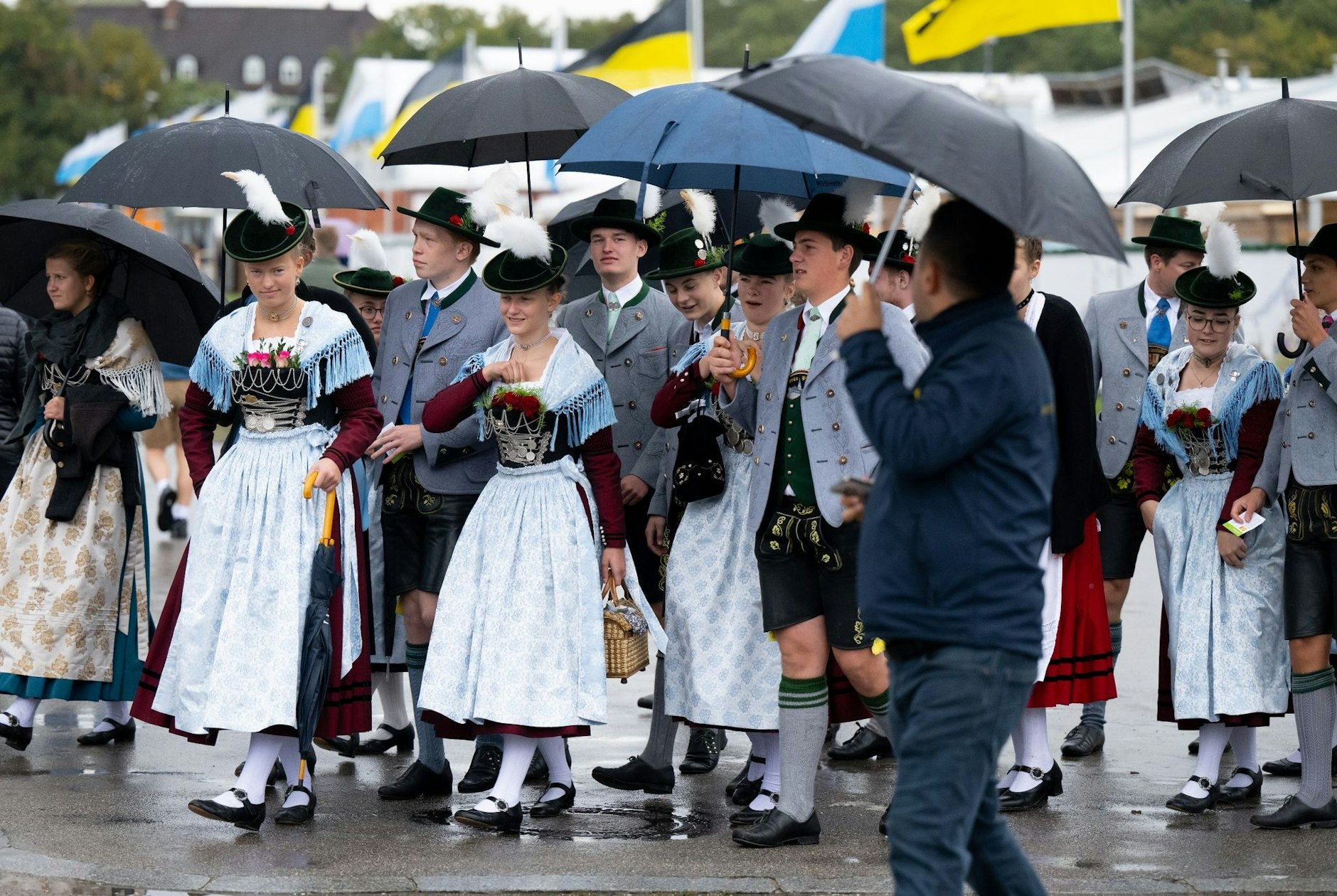 Eine Trachtengruppe geht nach dem traditionellen Trachten- und Schützenzug mit Regenschirmen über das Oktoberfestgelände.  
