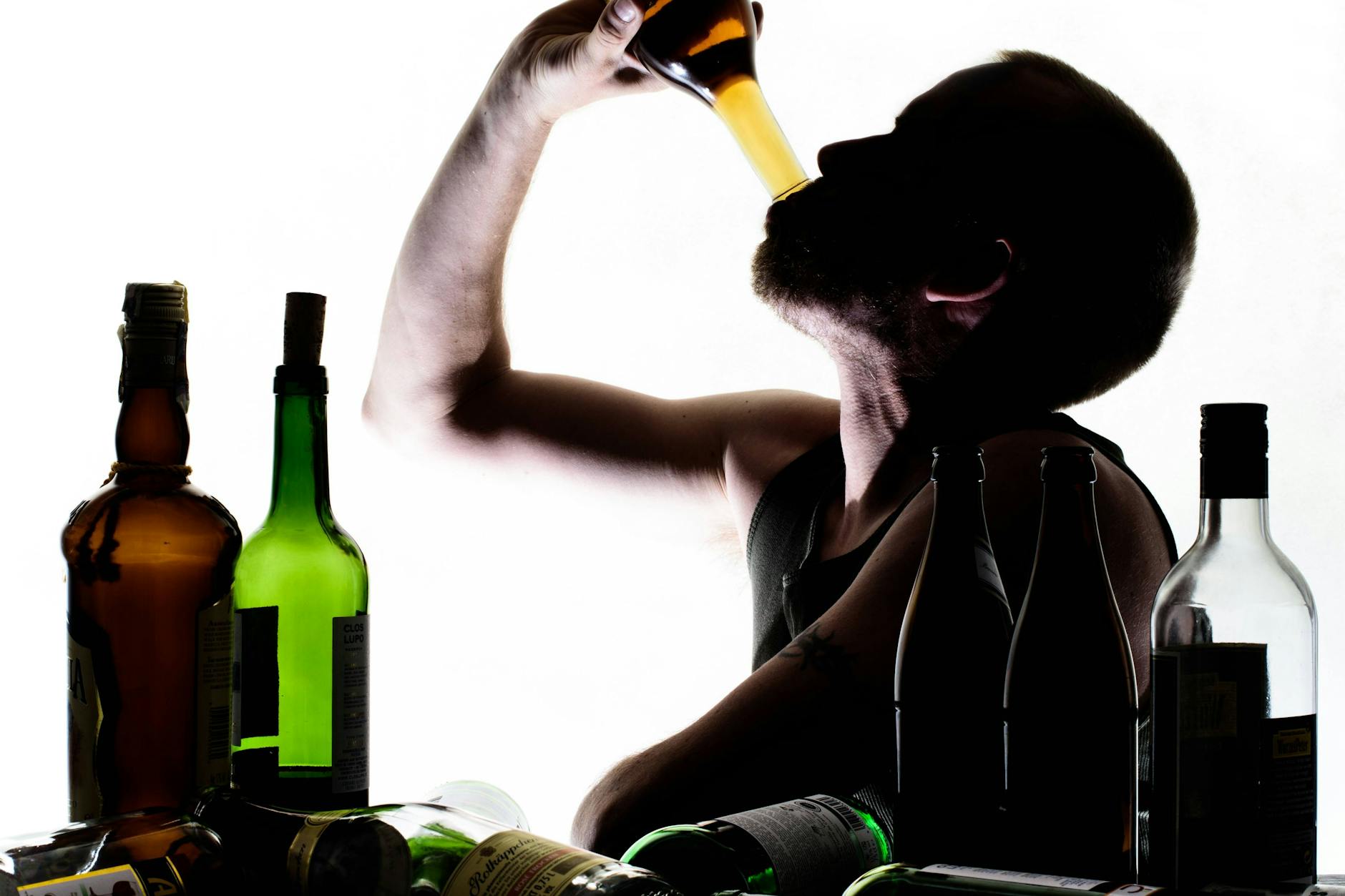 Ein Mann sitzt an einem Tisch mit leeren Flaschen Schnaps, Bier, Sekt und Wein. Aber welcher Alkohol macht eigentlich schneller betrunken und welcher wie dick?