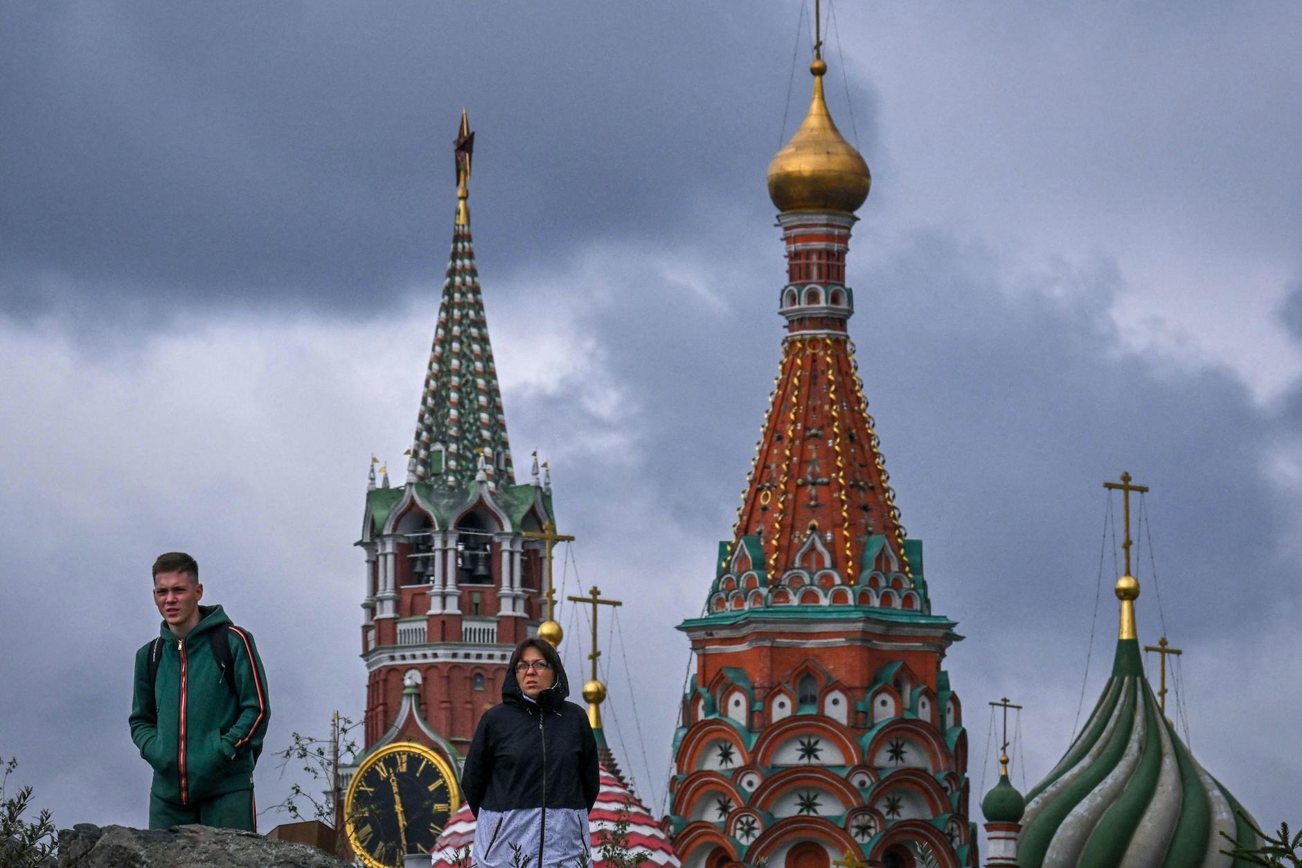 Spaziergänger im Zaryadye-Park vor dem Spasskaya-Turm des Kremls (L) und der Basilius-Kathedrale in Moskau.