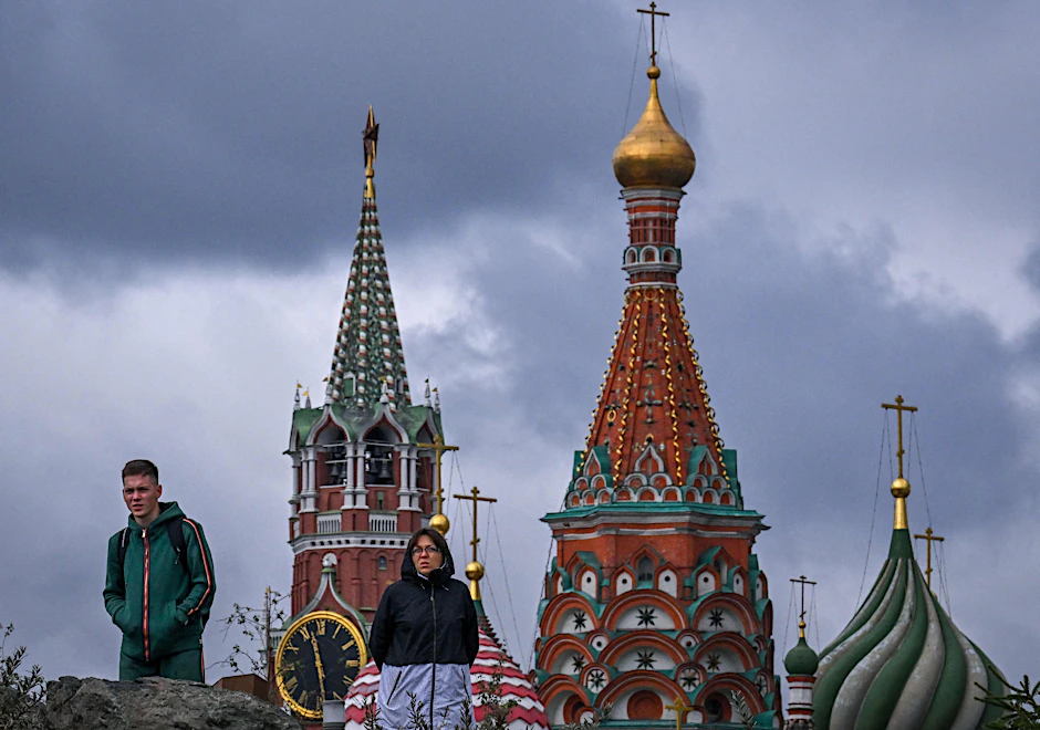 Spaziergänger im Zaryadye-Park vor dem Spasskaya-Turm des Kremls (L) und der Basilius-Kathedrale in Moskau.