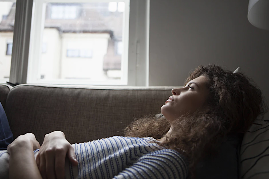 Eine Frau liegt besorgt auf ihrer Couch. (Symbolbild)
