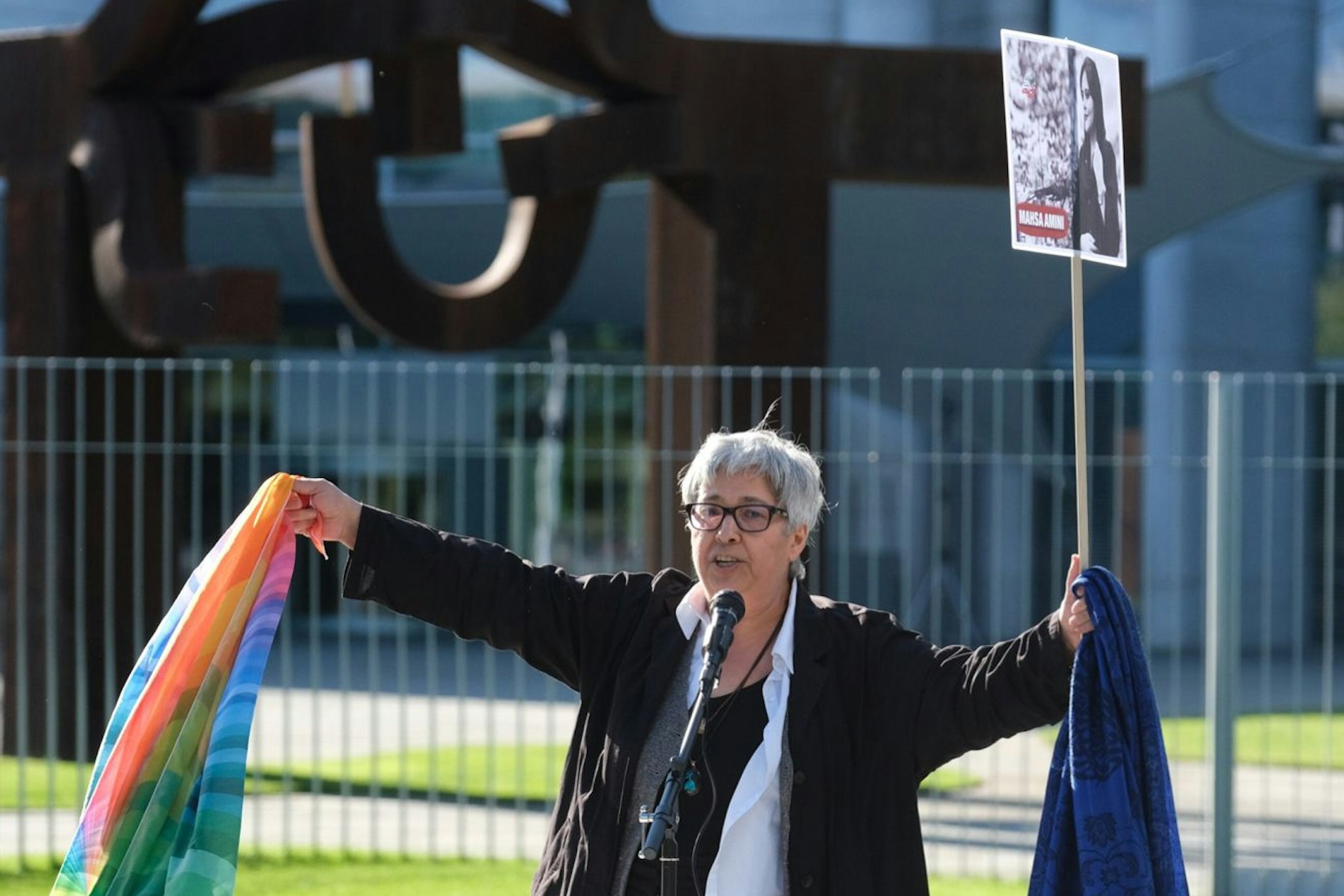 Seyran Ateş mit einem Kopftuch in der linken und eine Regenbogenfahne in der rechten Hand bei der Kundgebung vor dem Kanzleramt.