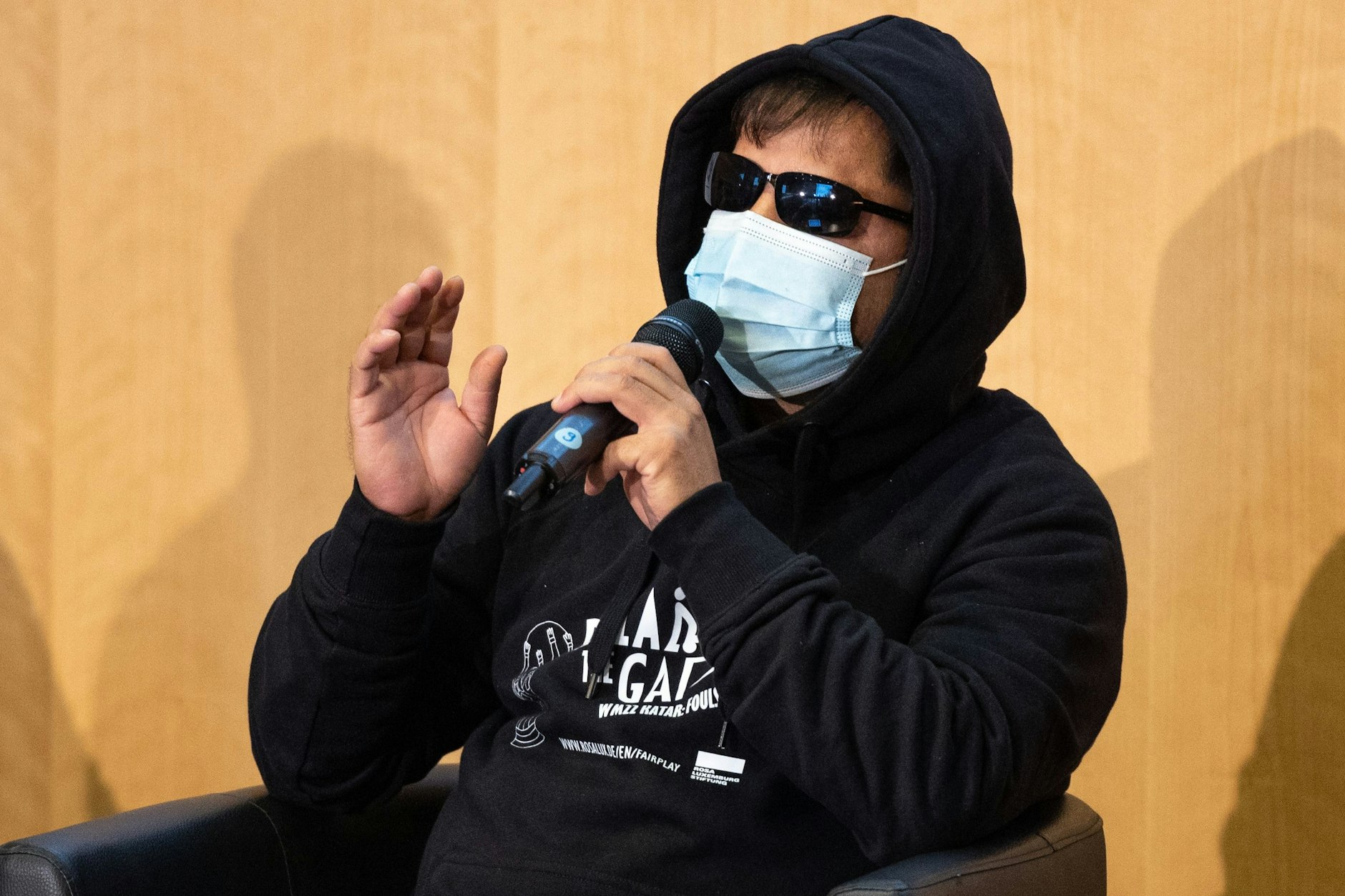 Ein ehemaliger Arbeiter in Katar berichtet während der Gesprächsrunde „Katar 2022. Nicht unsere WM!“ in Frankfurt. Zum Schutz seiner Identität trägt er Sonnenbrille und Kapuzenpulli.