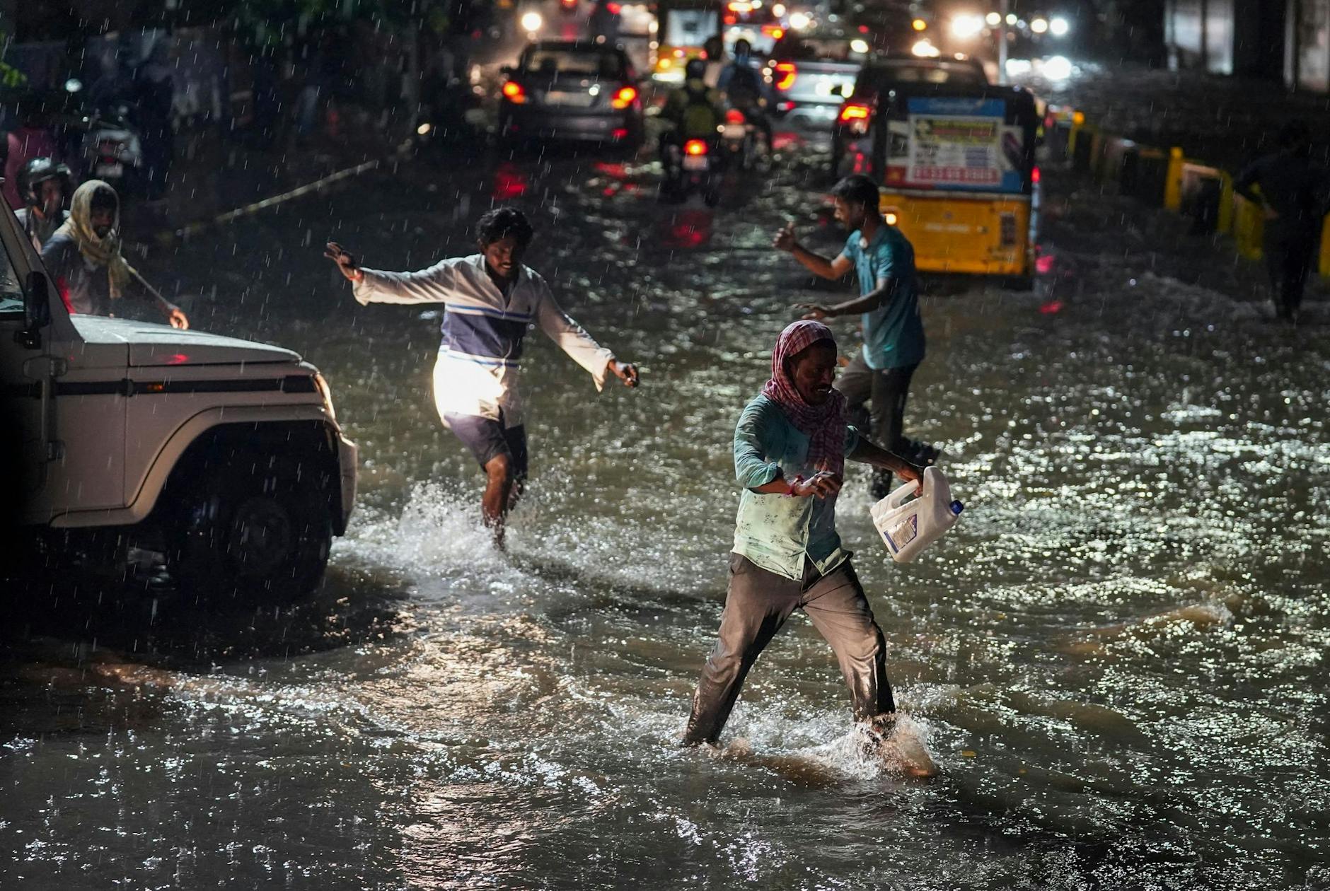 Passanten waten während starker Regenfälle durch eine mit Wasser vollgelaufene Straße in Indien.