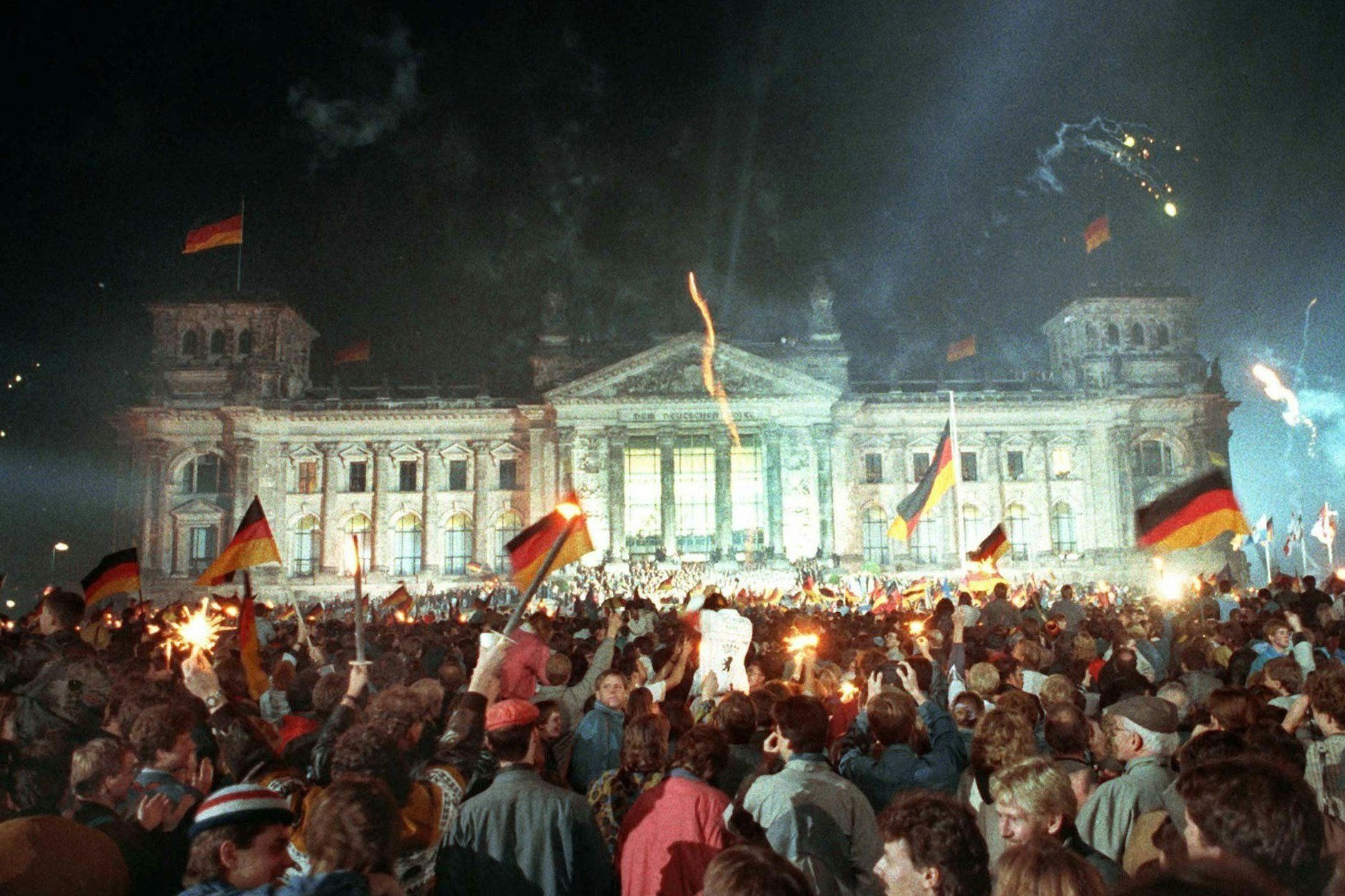 Menschen jubeln mit schwarz-rot-goldenen Fahnen, als in der Nacht zum 3. Oktober 1990 vor dem Reichstag in Berlin die Wiedervereinigung Deutschlands vollzogen wurde.