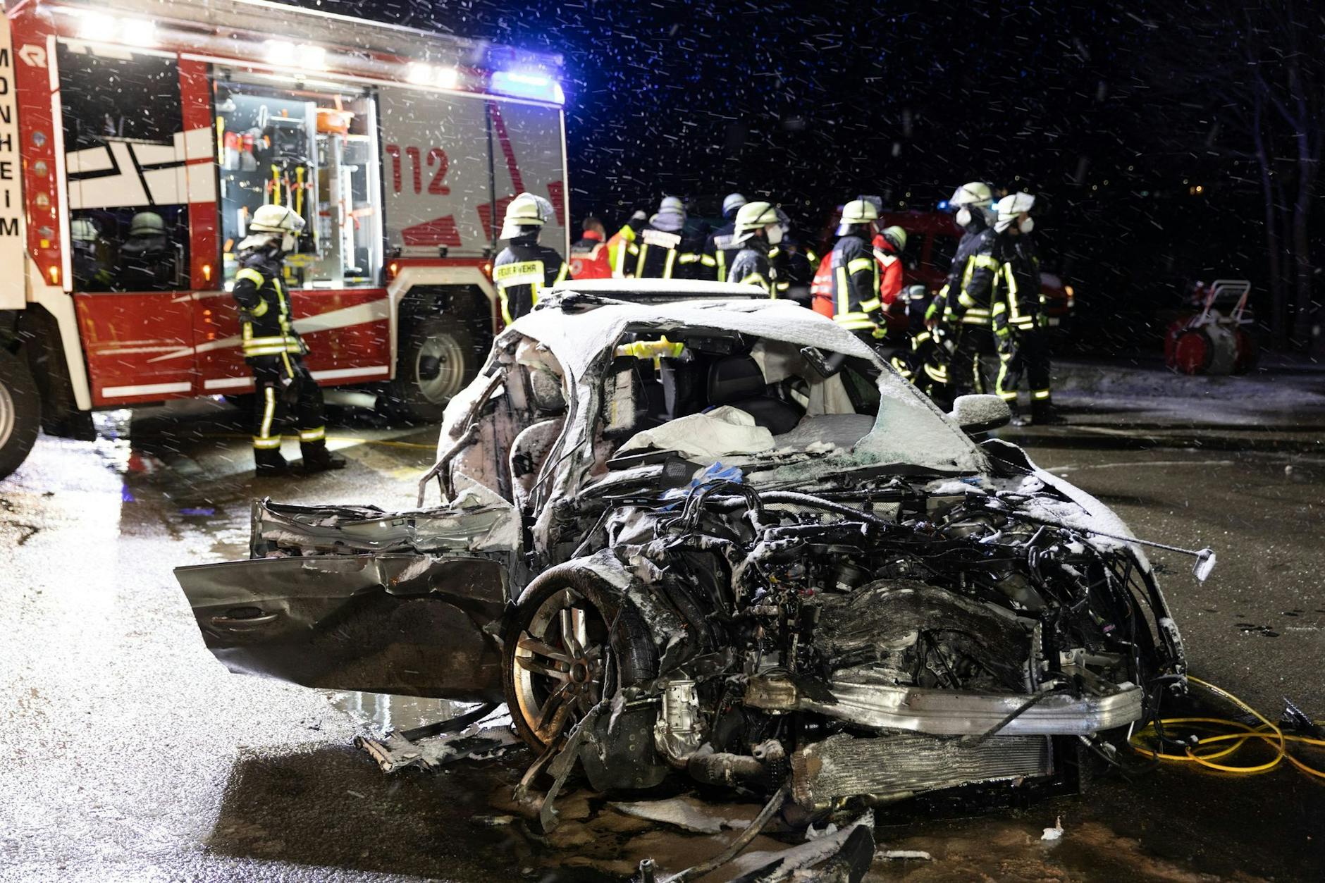 ARCHIV - Feuerwehrleute stehen im April 2022 bei Monheim nach der Kollision hinter dem Autowrack einer 54 Jahre alten Frau. Sie starb noch am Unfallort.