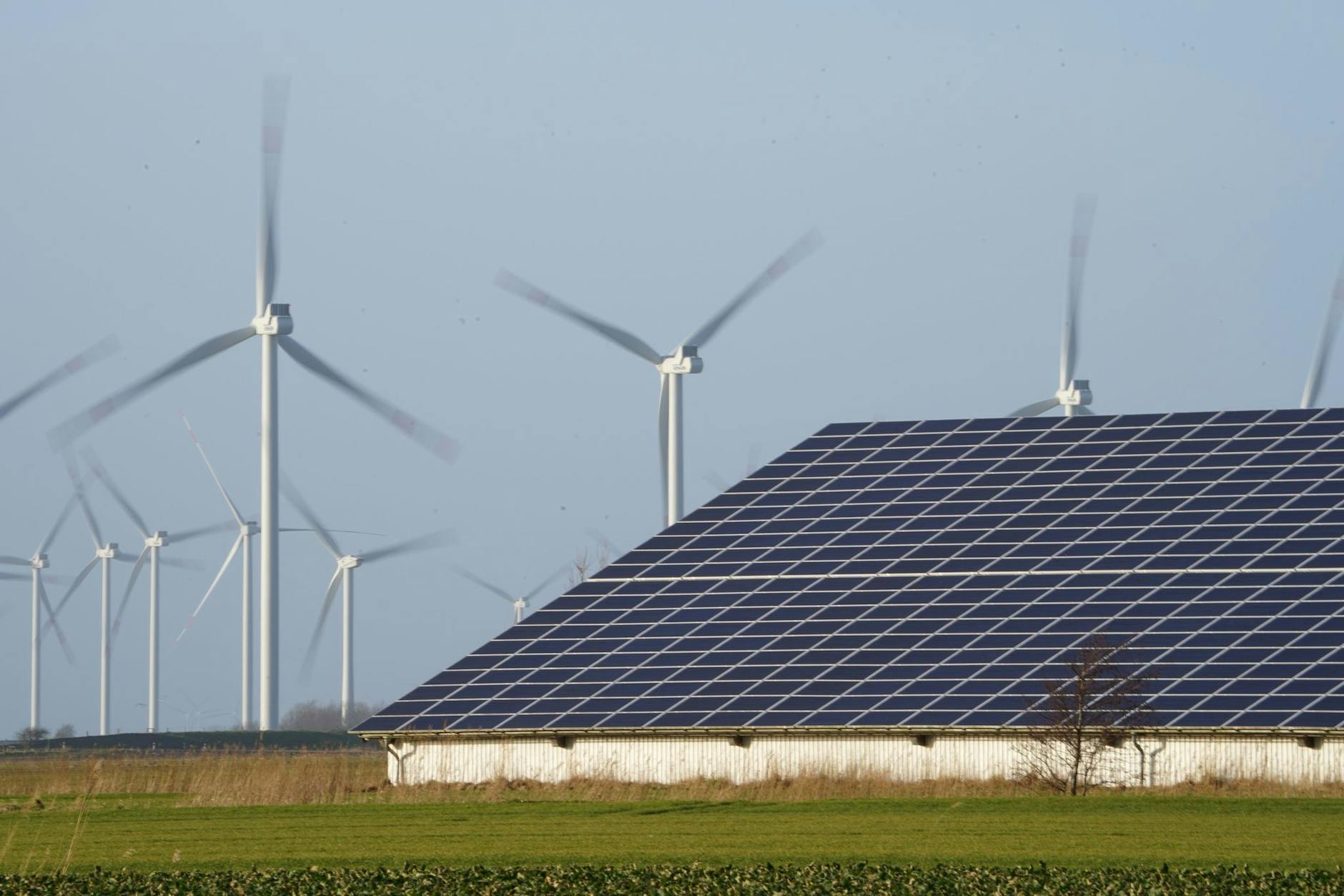 ARCHIV - Windenergieanlagen stehen neben einer Halle mit Photovoltaik-Anlagen.