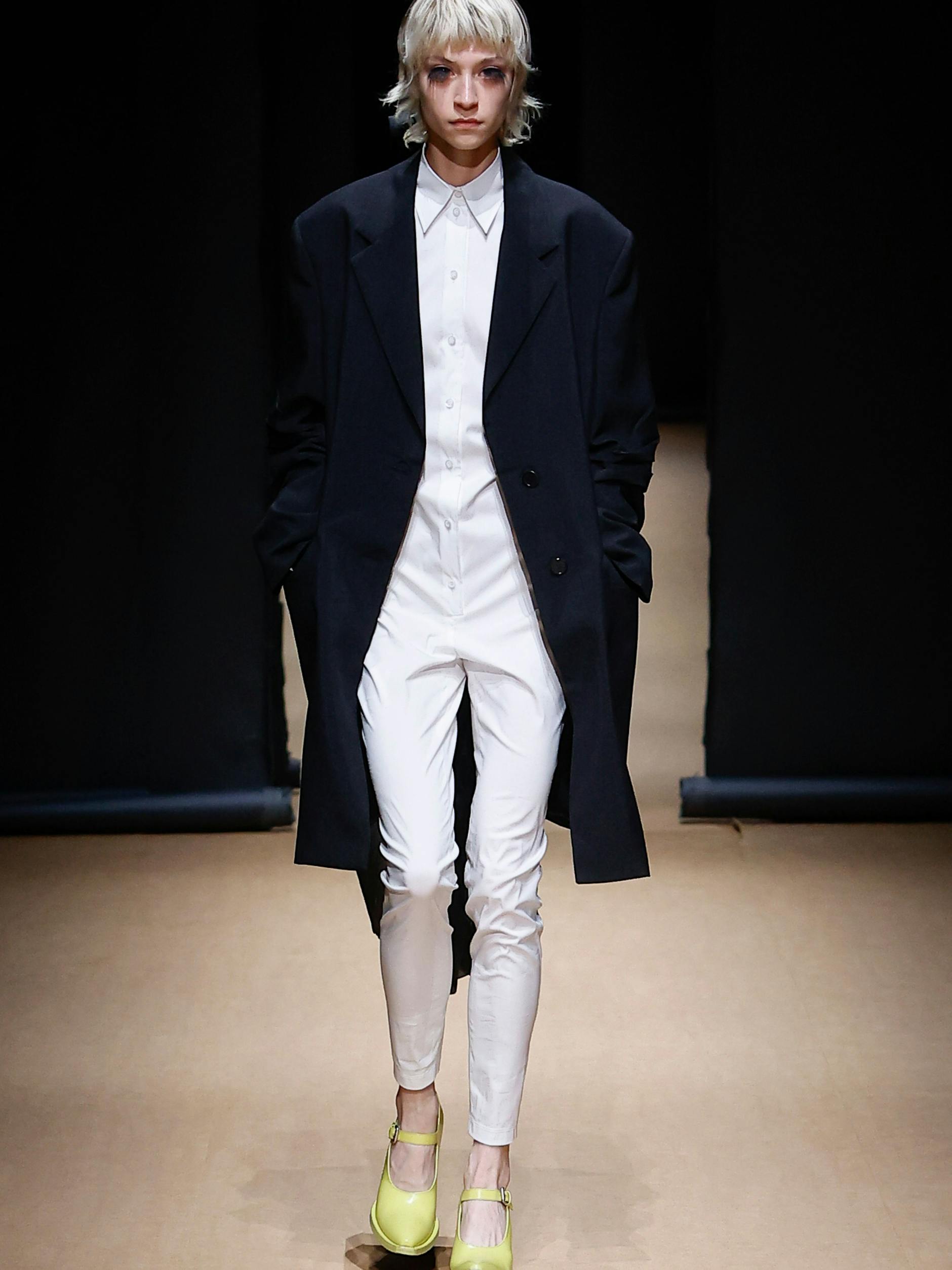 Von Prada: ein weißer Onesie in laborhaft-disziplinärer Strenge, darüber ein Mantel mit verkürzter Schleppe.