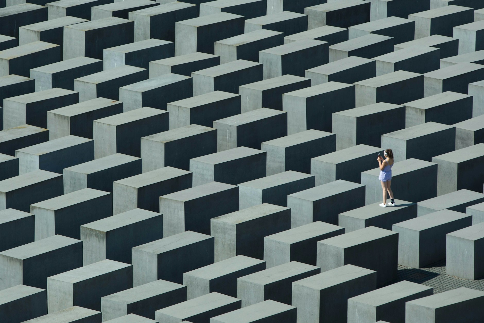 Eine Besucherin des Holocaust-Mahnmals in Berlin steht bei hochsommerlichen Temperaturen auf einer der Stelen und fotografiert.