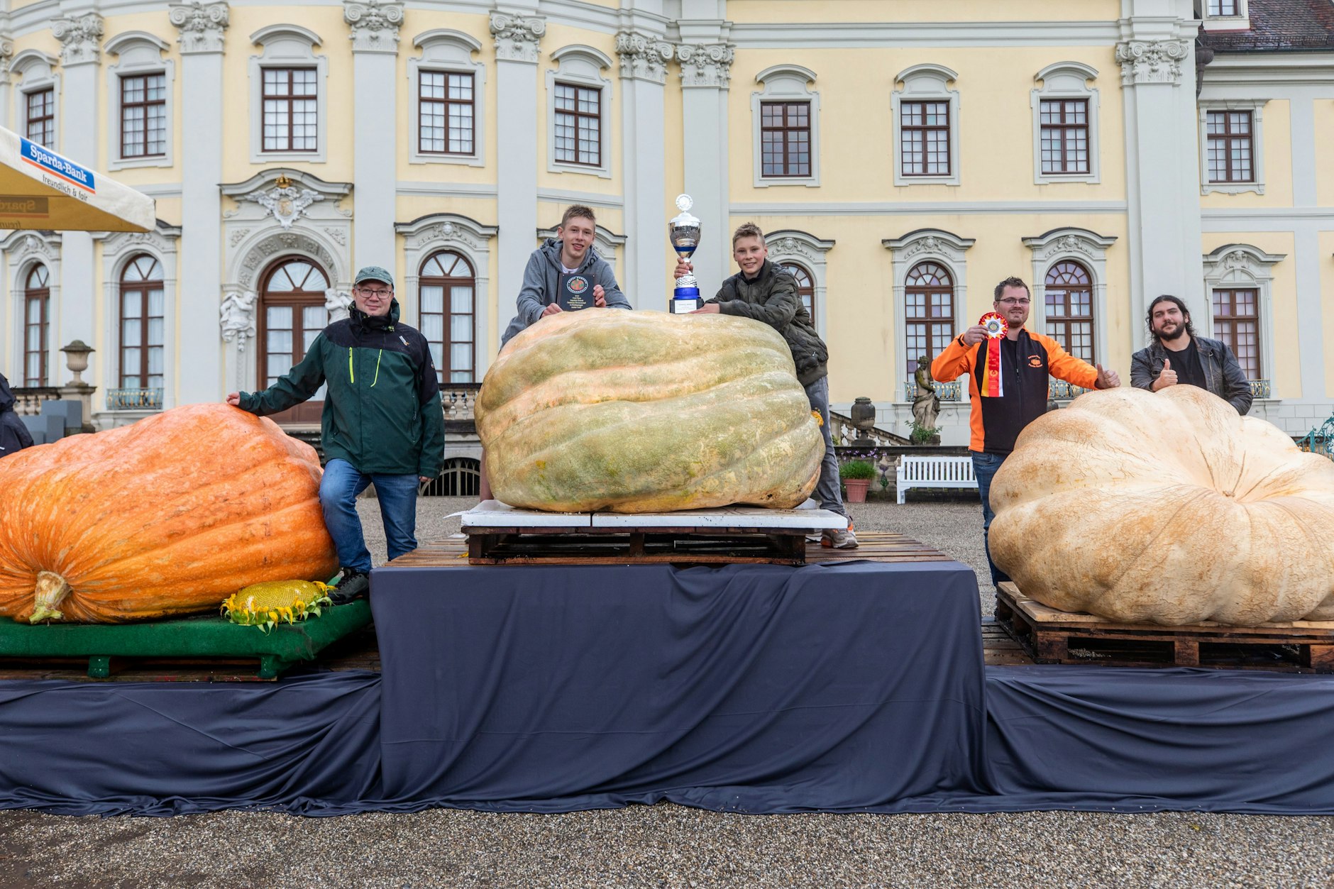 Die drei schwersten Kürbisse der deutschen Meisterschaft im Kürbiswiegen mit ihren Züchtern: Auf Platz 3, Kevin Kloch (2. v. r.) und Marius Weishäupl (r.) und ihr 746 Kilogramm schwerer Kürbis; Platz 2, Matthias Würsching (l.) mit seinem 754 Kilogramm schweren Kürbis und Platz 1 für Jakob (2. v. l.) und David Frommelt mit ihrem 796 Kilogramm schweren Kürbis.&nbsp;